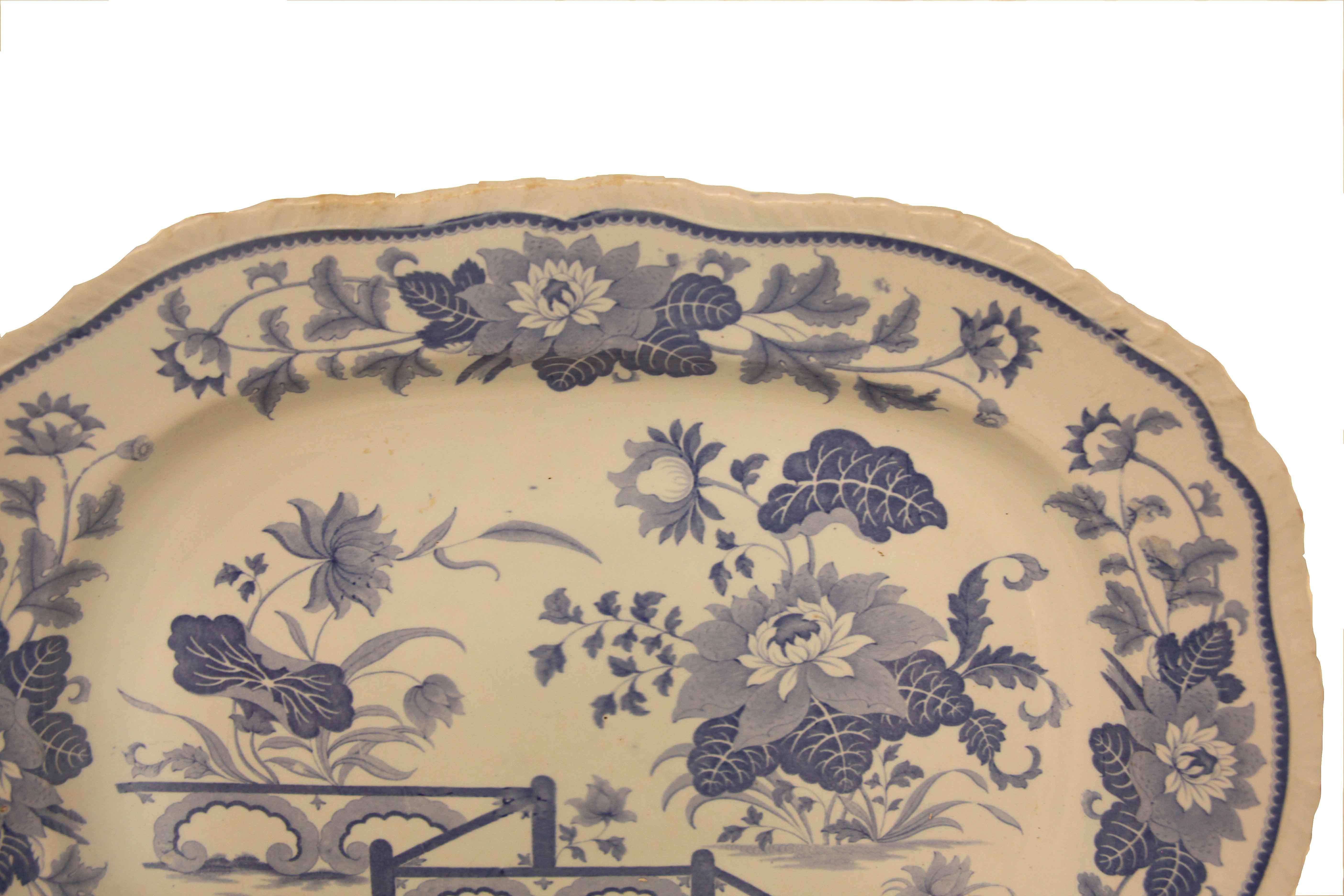 Blue and white ironstone platter, the rim has an undulating shape with ''ribbing'' along the edge,  the inner border has a repeating design of a central flower and foliate with trailing foliate and flowers on each end.  The main body features larger
