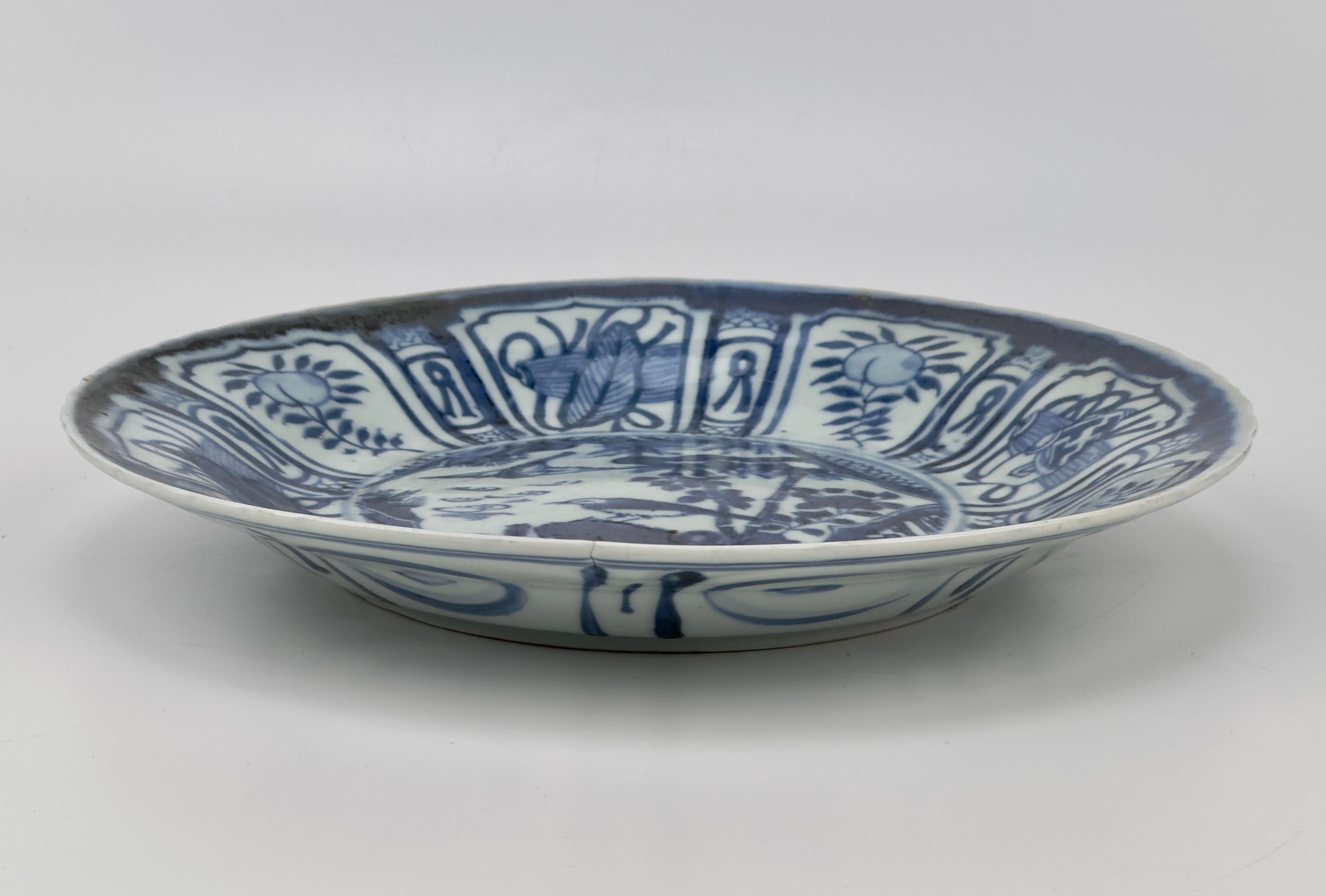 A Chinese blue and white Kraak plate, the central roundel depicting birds and floral design in a waterside, the rim with panels enclosing foliage and decorative objects.

Period: Late Ming-Early Qing Dynasty (17th century)
Type: Blue and White