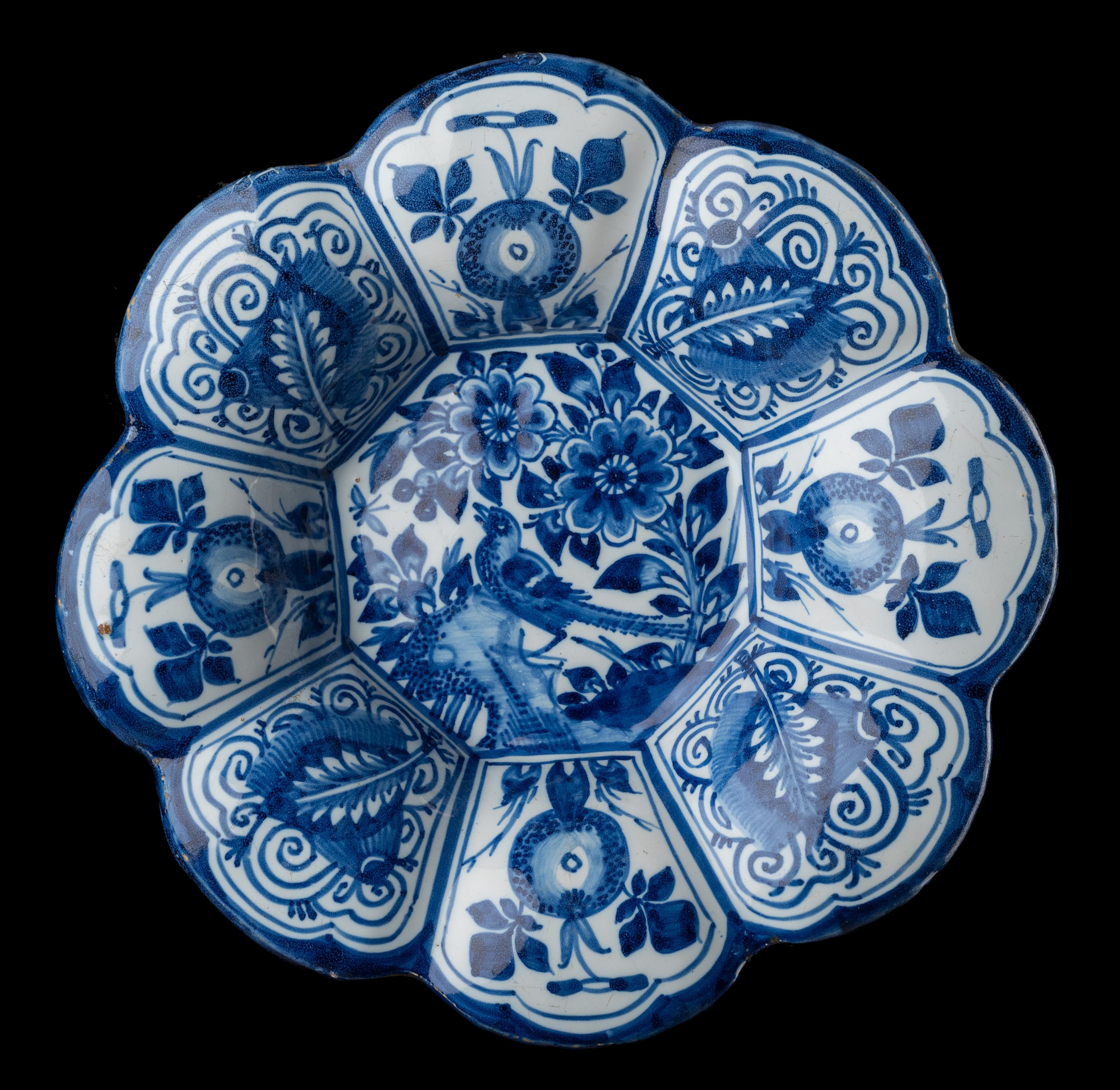 Blue and white chinoiserie lobed dish Delft, circa 1680.

The lobed dish is composed of eight wide lobes and is painted in the centre in blue with a chinoiserie landscape of a bird on a rock with flowers. The lobes are alternately decorated with a