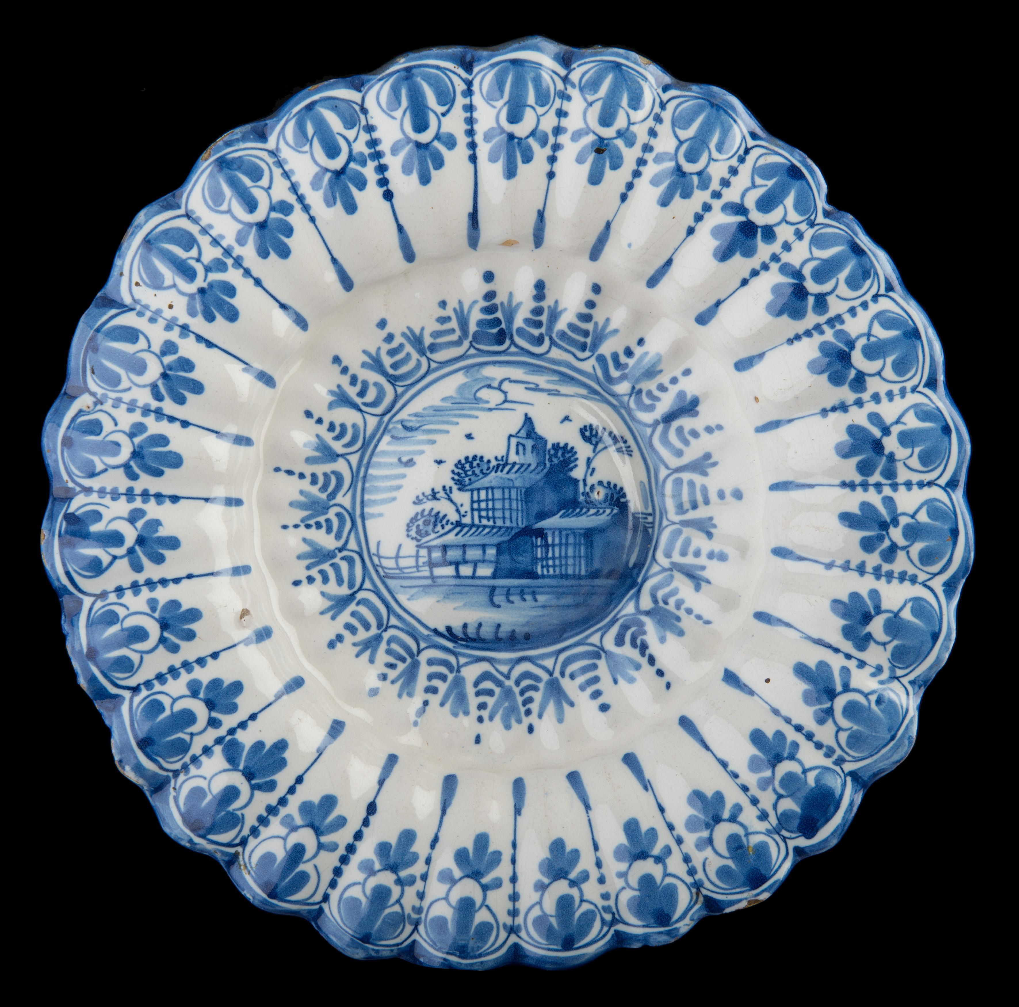 Blue and white lobed dish with landscape. Northern Netherlands, 1640-1660.
Dimensions: diameter 29,1 cm / 11.41 in.

The blue and white dish is composed of twenty-seven double lobes. The curved center is painted with a simplified landscape within