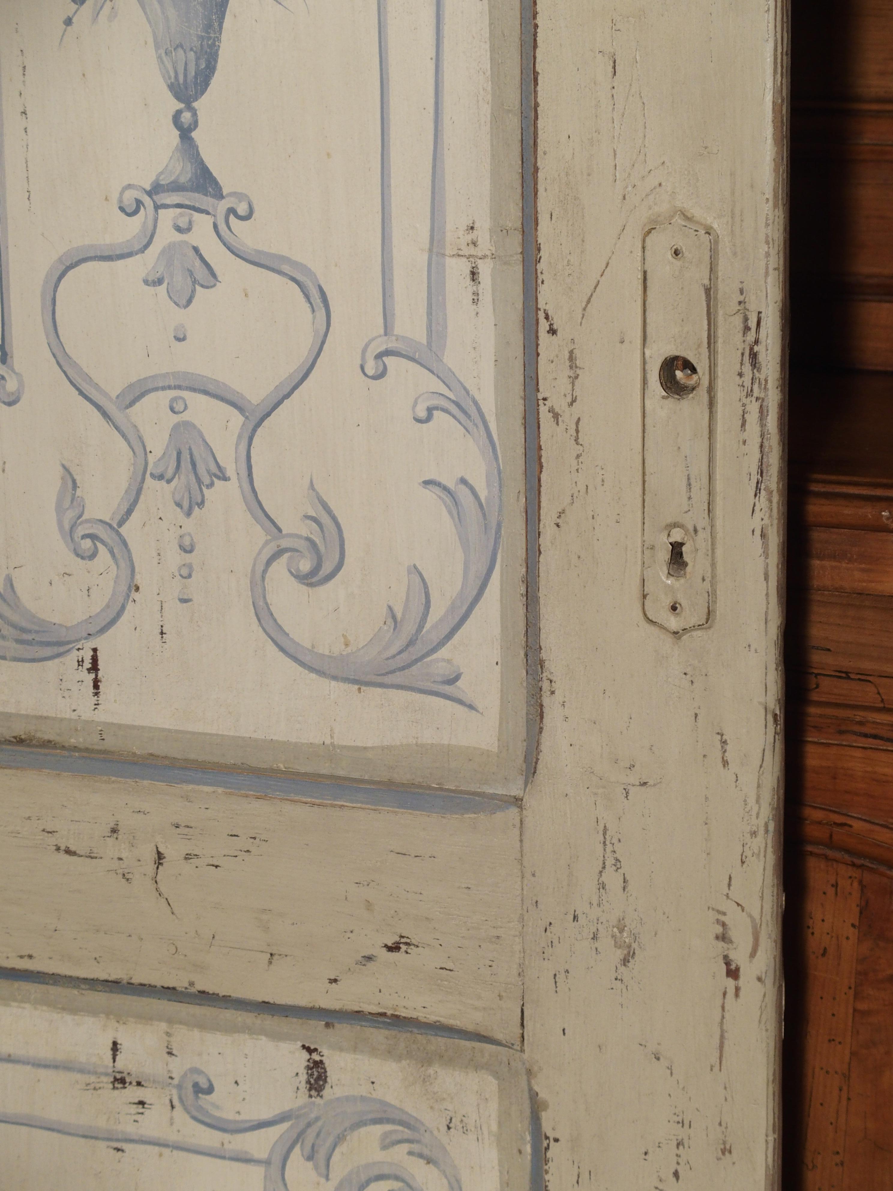 This paneled and double sided interior door was hand painted in Lombardy, Italy circa 1850. Both sides have the same paneling and decoration. The upper two vertical, raised panels have hand painted, delicate neoclassical floral designs. The center