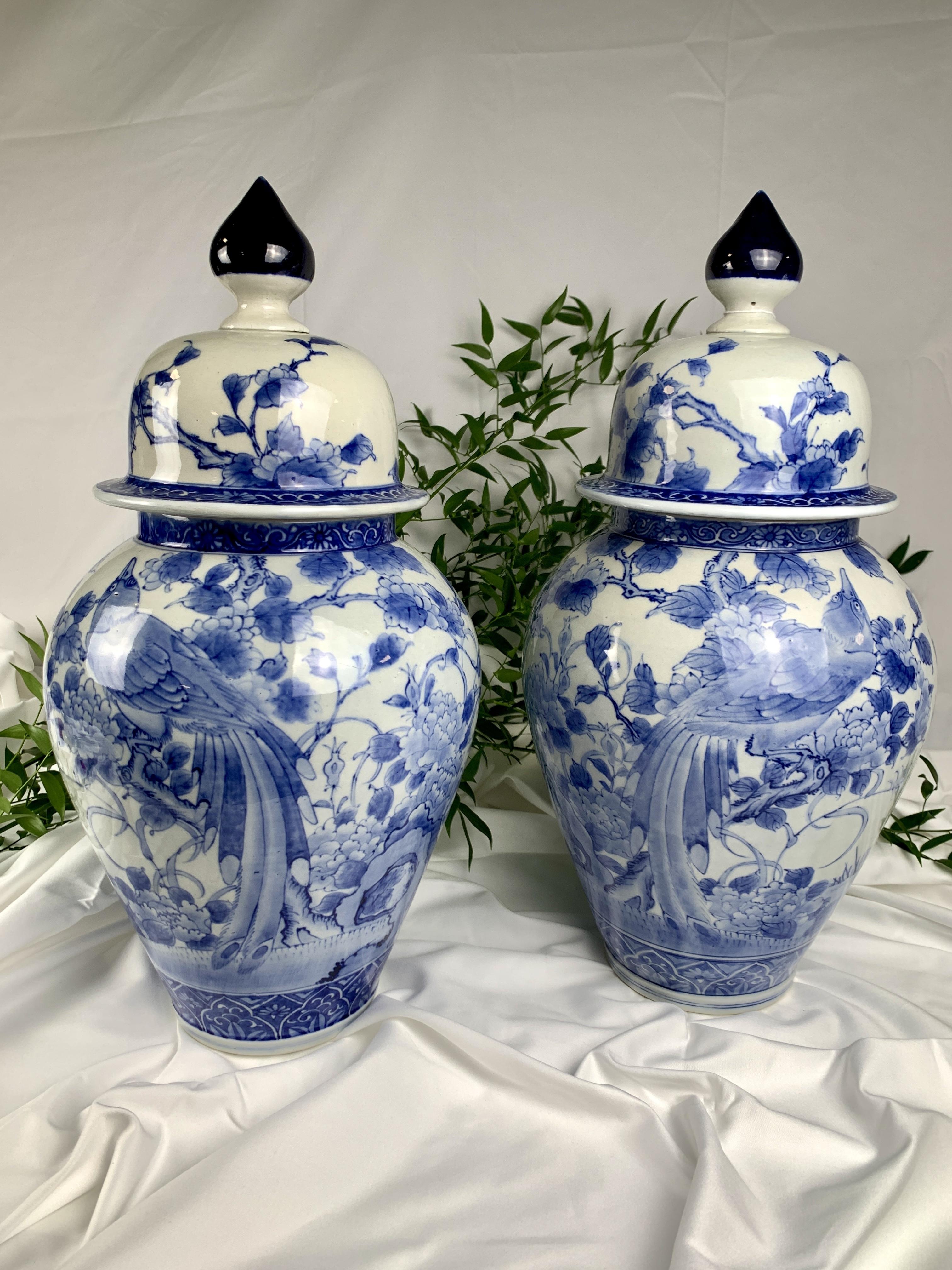 This pair of large jars has refined blue and white hand-painted decoration that showcases a songbird perched on a flowering tree. Above, two birds are depicted in flight.
The jars are mirror images of each other. 
The painter used an underglaze of