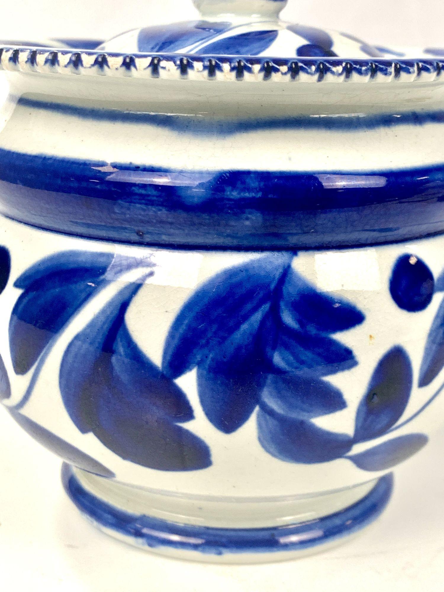 This lovely blue and white pearlware pottery sugar box is decorated with three beautiful patterns of leaves and berries. The body, the top edge around the cover, and the cover each have a similar but slightly different pattern. The edge of the sugar