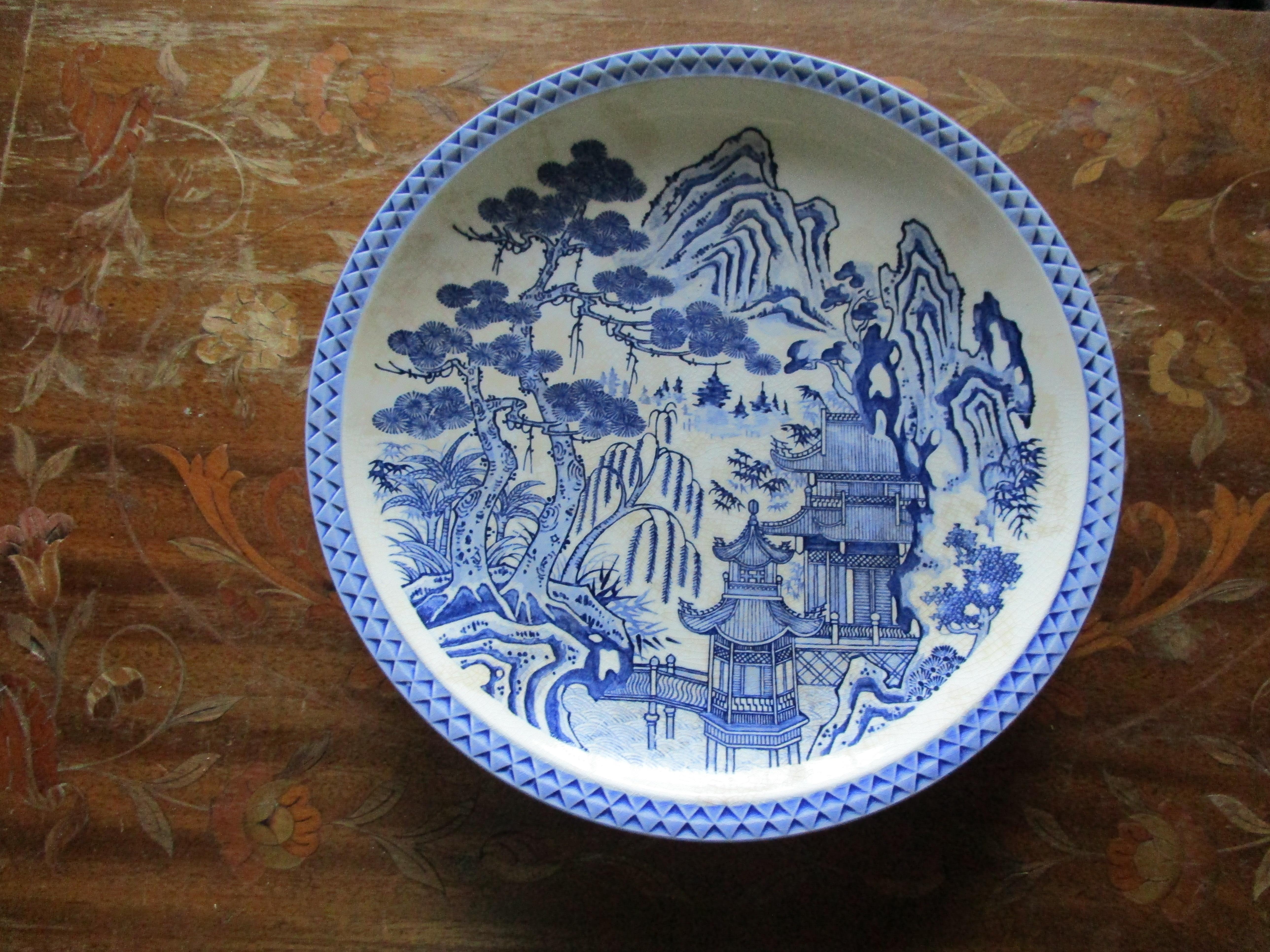 This is a rare blue and white porcelain charger/plate that is 12 inches in diameter. The backdrop is detailed with a pagoda, a footbridge, mountains and a whimsical blue willow tree. This vintage Chinese export blue and white porcelain charger 
is