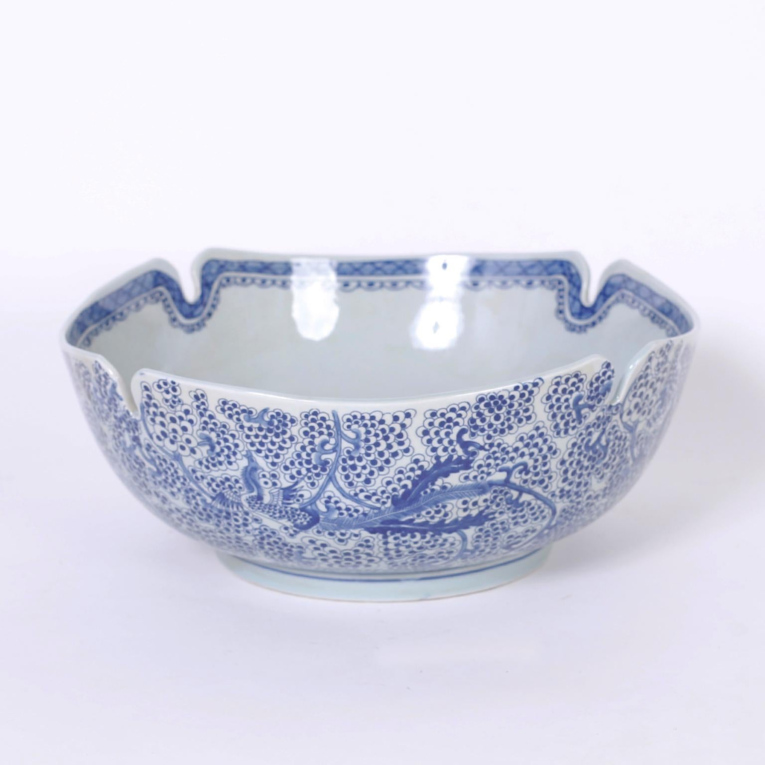 Blue and white Chinese porcelain bowl hand decorated with phoenix birds over a floral background and featuring an unusual scalloped and slotted rim.
 