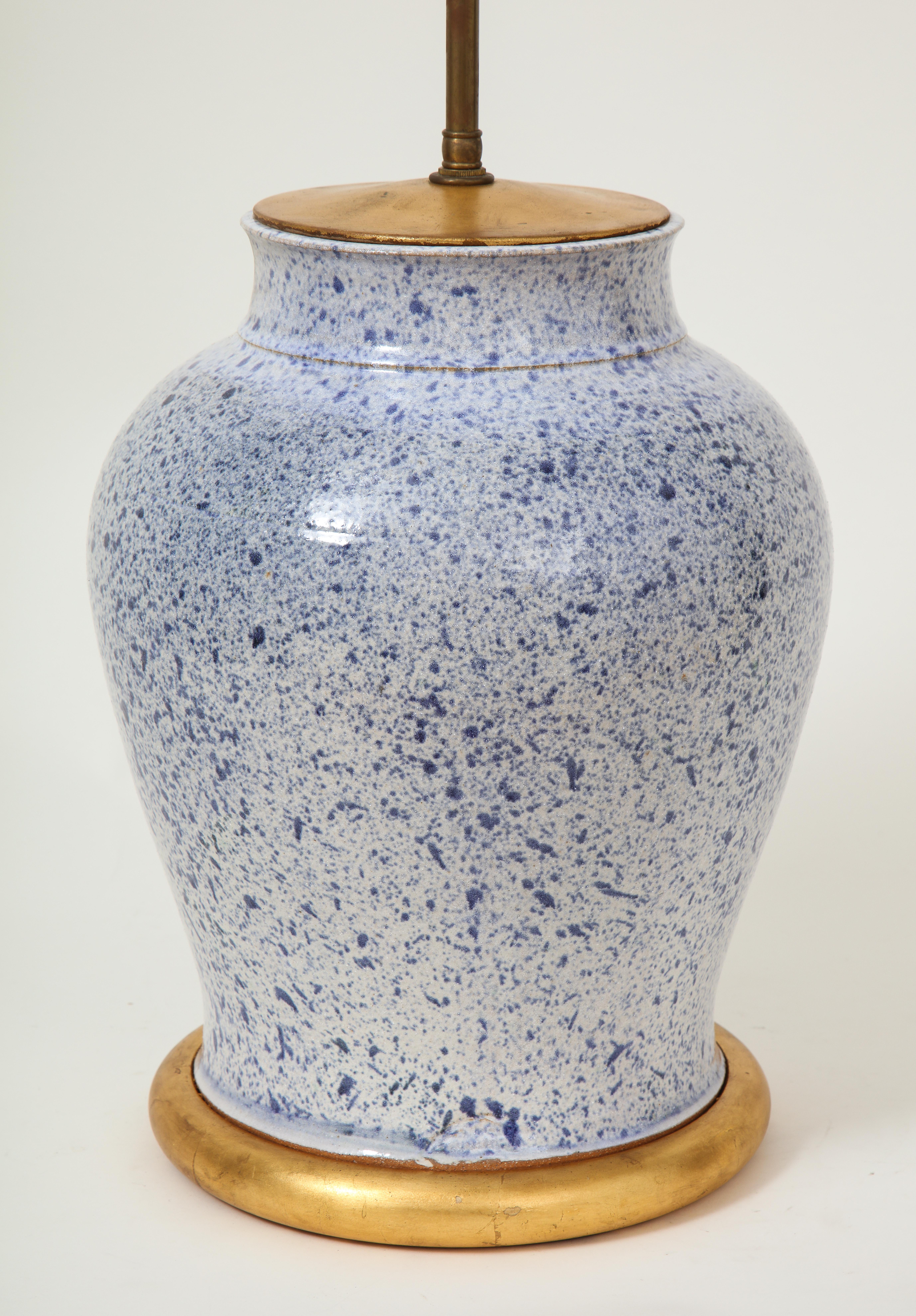 The baluster form ceramic base spattered overall in blue glaze; mounted on a gilt base; fitted with an adjustable rod and two light sockets. Height to top of vase is 15.5