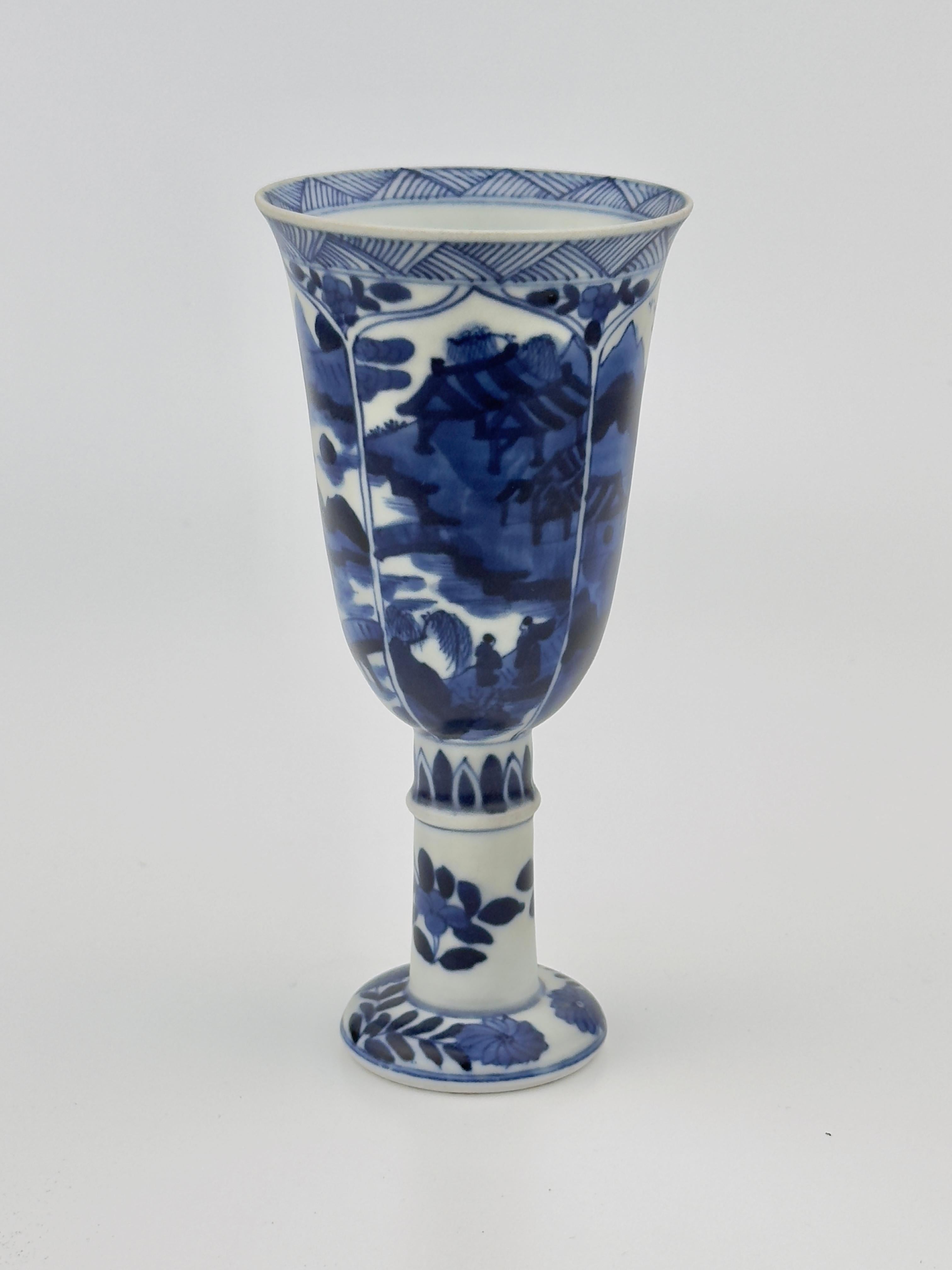 This porcelain stemcup has a domed foot, a high stem and an elongated deep bowl with a partially broken flared rim. River landscapes featuring trees, pavilions, bridges and figures, are painted in four vertical panels in underglaze blue. Used for