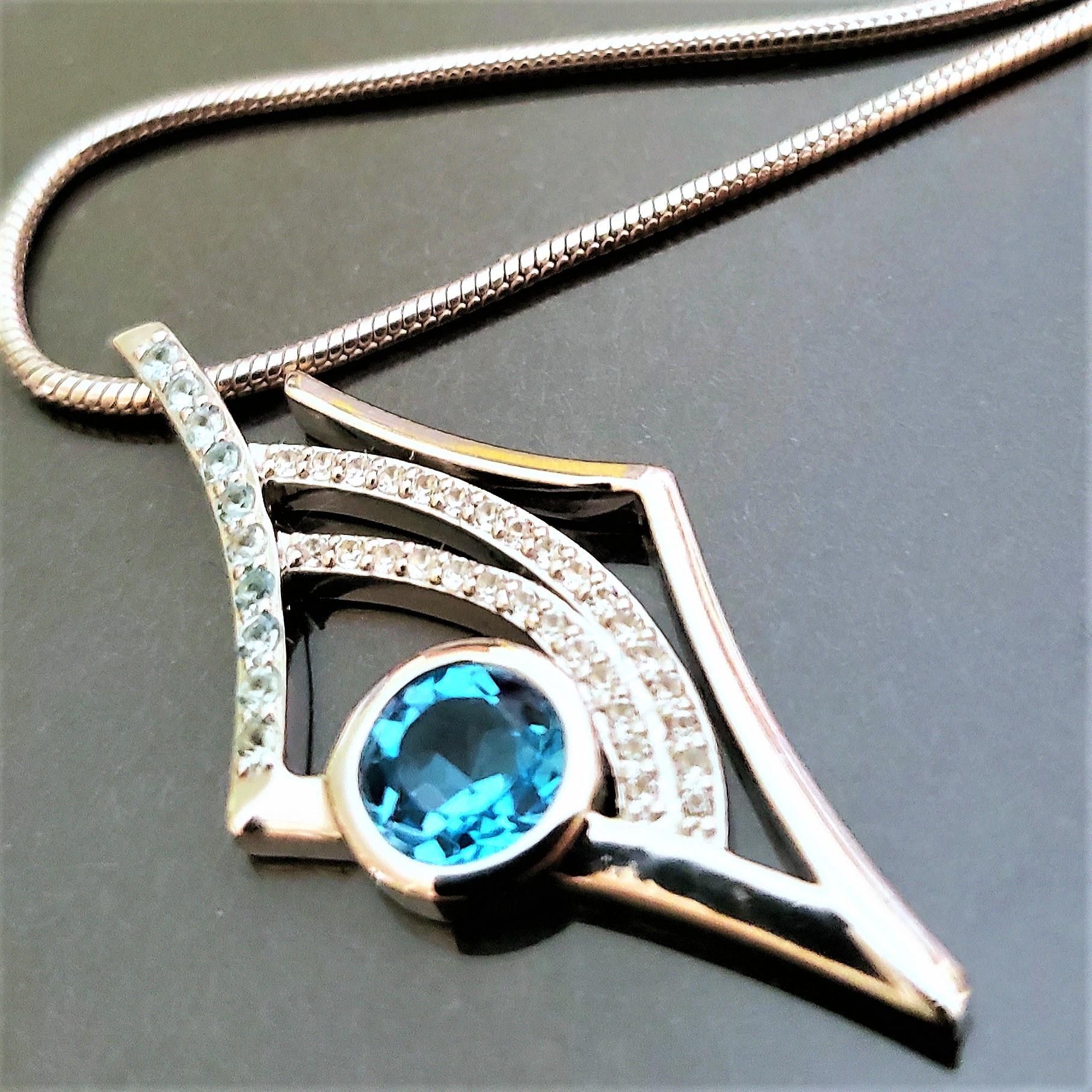 Der Anhänger Antares Origins aus Sterlingsilber (8,94 g) ist mit einem funkelnden 6 mm großen Schweizer Blautopas besetzt. Dieser Stein ist von einem wunderschönen blau und weiß funkelnden Topas umgeben. Es gibt dreißig - 1mm  steine und zehn 1,4 mm