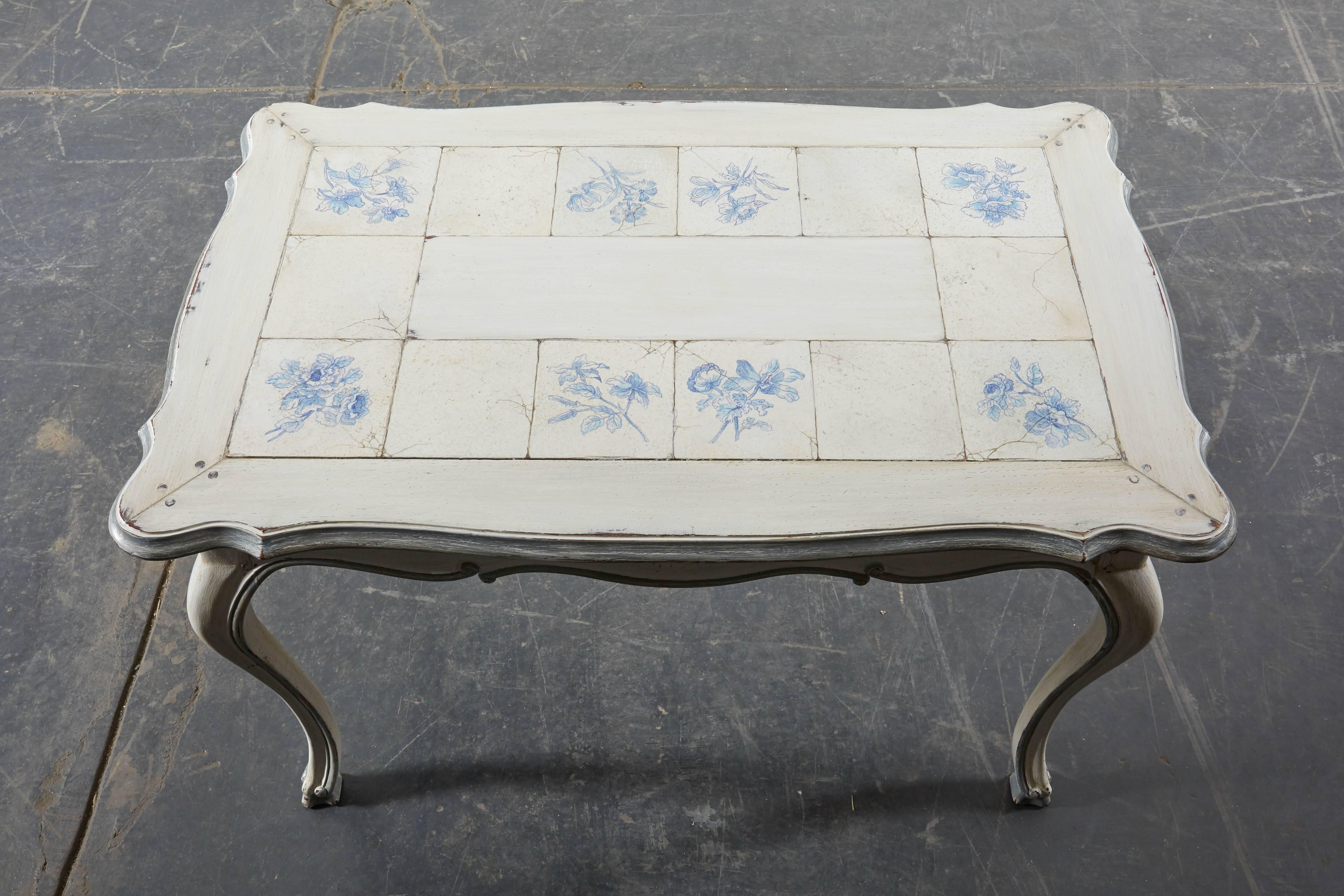 The rectangular top with scalloped edge finely painted to look like antique delft tiles complete with faux craquelure; raised on cabriole legs; painted an antique white with pale blue detailing.