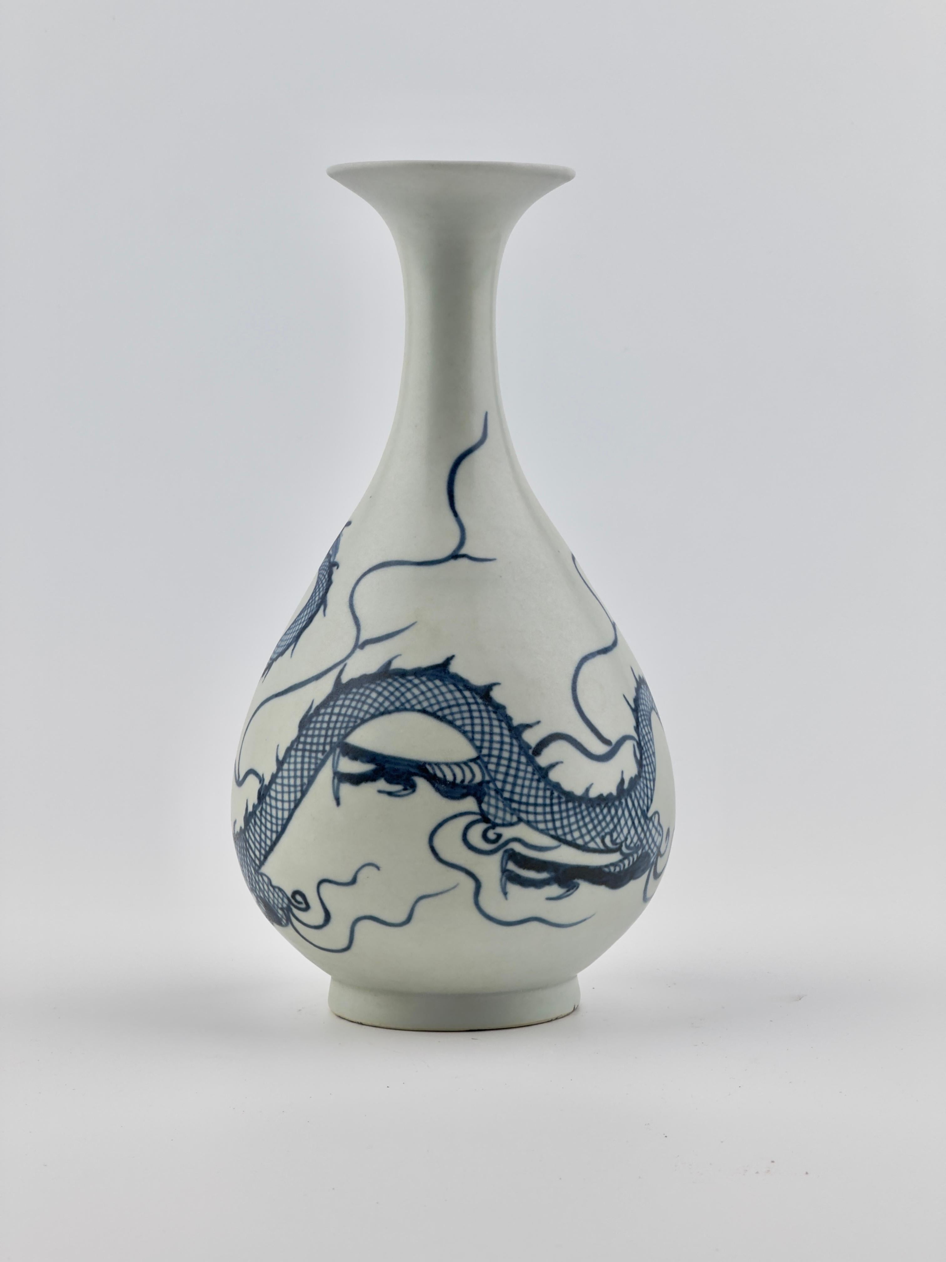 The vase is delicately potted featuring a pear-shaped body that rests on a slightly flared foot and extends upward into a trumpet-shaped neck. Its exterior showcases a dynamic, three-clawed dragon in stride amidst flames.

This piece reflects a