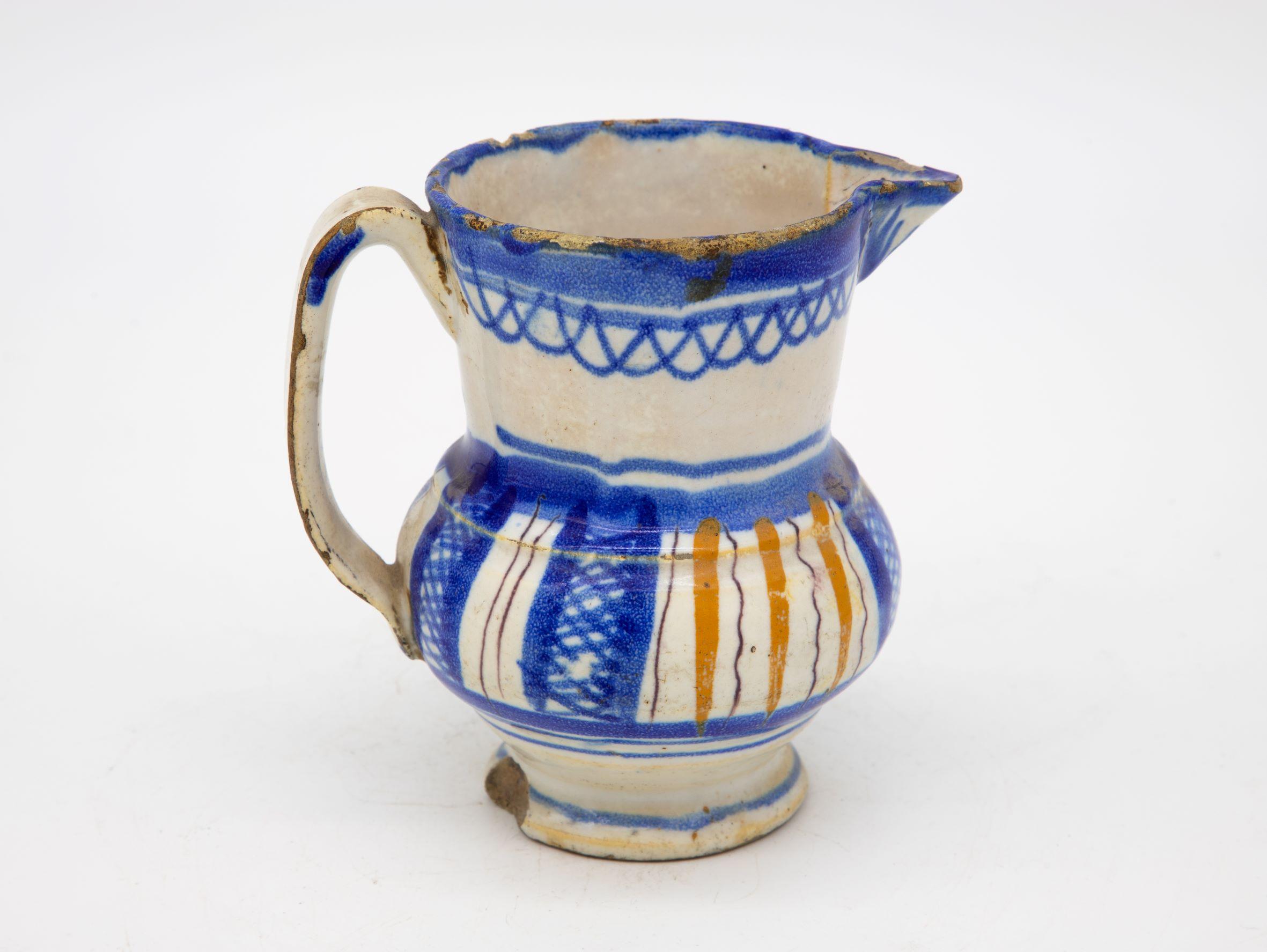 A small white ceramic pitcher or jug with blue and yellow stripe and decoration. Minor loss chips in the base and top. This petire pitcher is of unknown origin, but possibly Spanish. Late 19th century.