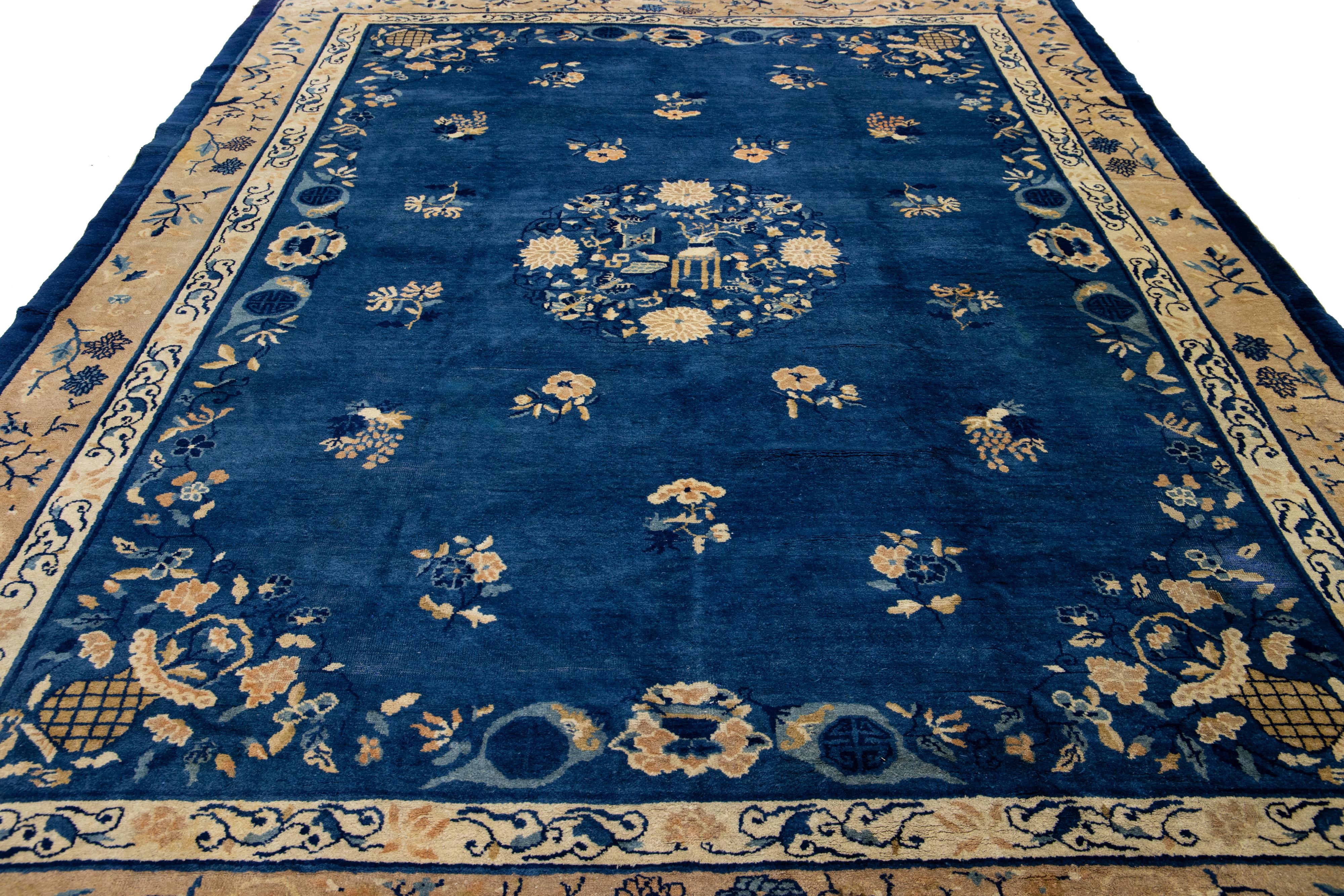 Cet exquis tapis antique chinois Art déco est soigneusement noué à la main avec de la laine de haute qualité. Il présente un fond bleu profond, rehaussé d'un élégant motif floral beige. Le motif est joliment encadré d'une bordure beige coordonnée,