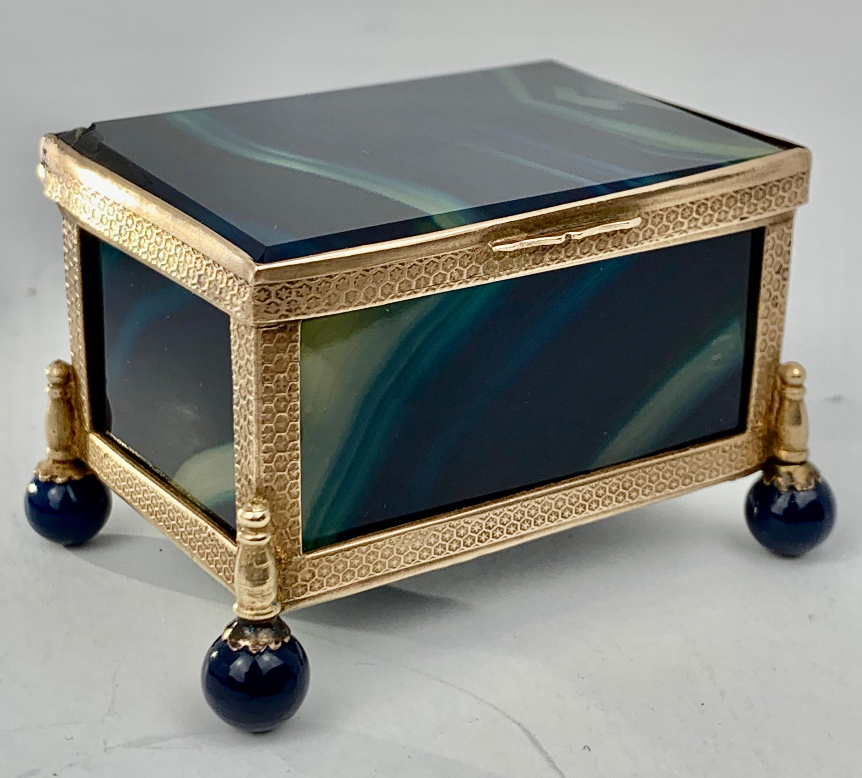 Stunning blue banded hinged agate box with gilt honeycomb patterned frame, the pieces of stone are beveled on the interior while the petit box rests on ball feet.  There is a tiny chip on the top back left corner.
How handsome the carefully selected