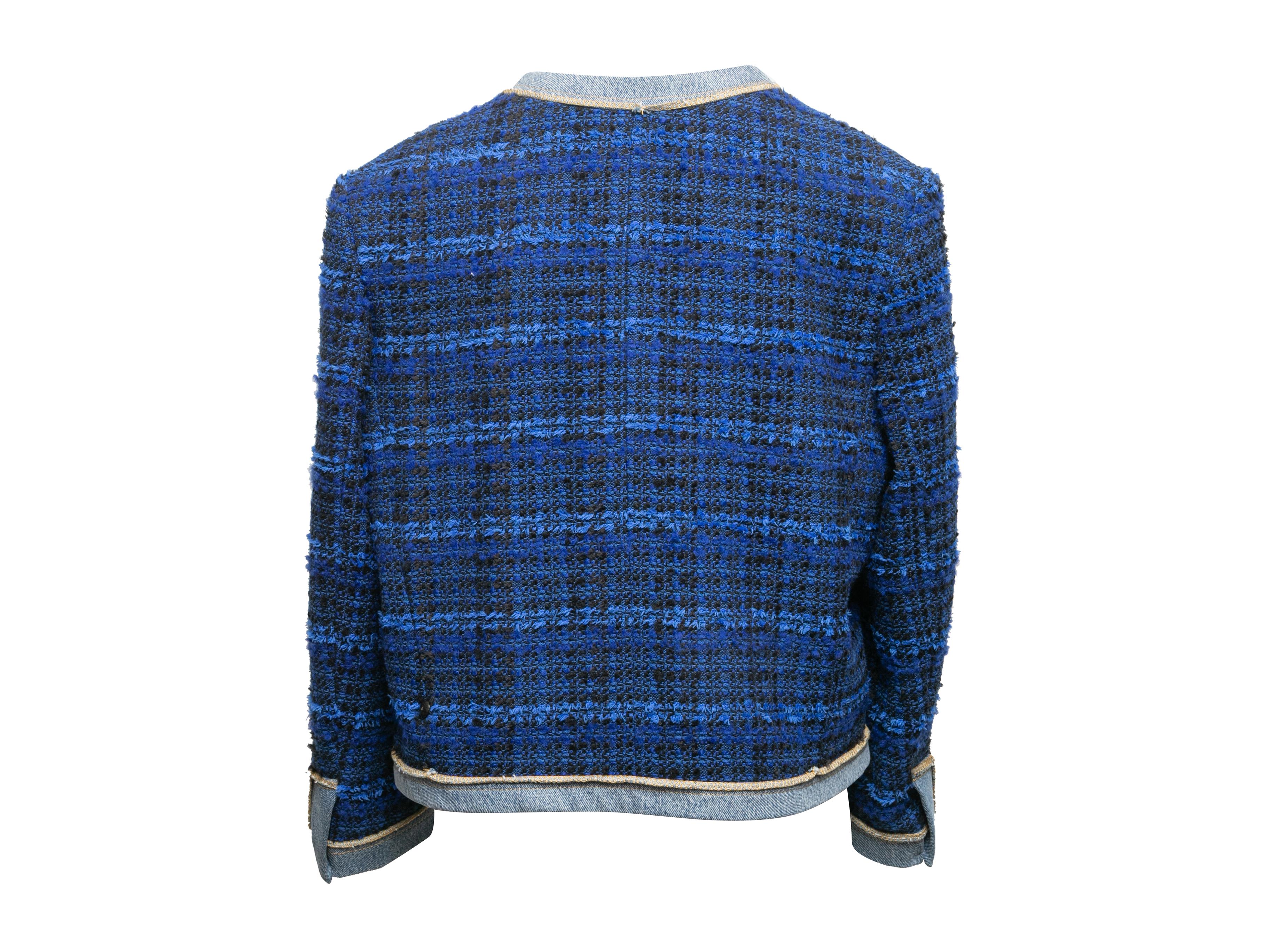Veste sans col en tweed bleu et noir de Sandro. Garniture en denim légèrement délavé sur l'ensemble du corps. Col ras du cou. Deux poches sur les hanches. Fermeture par boutons au centre du devant. Poitrine 40