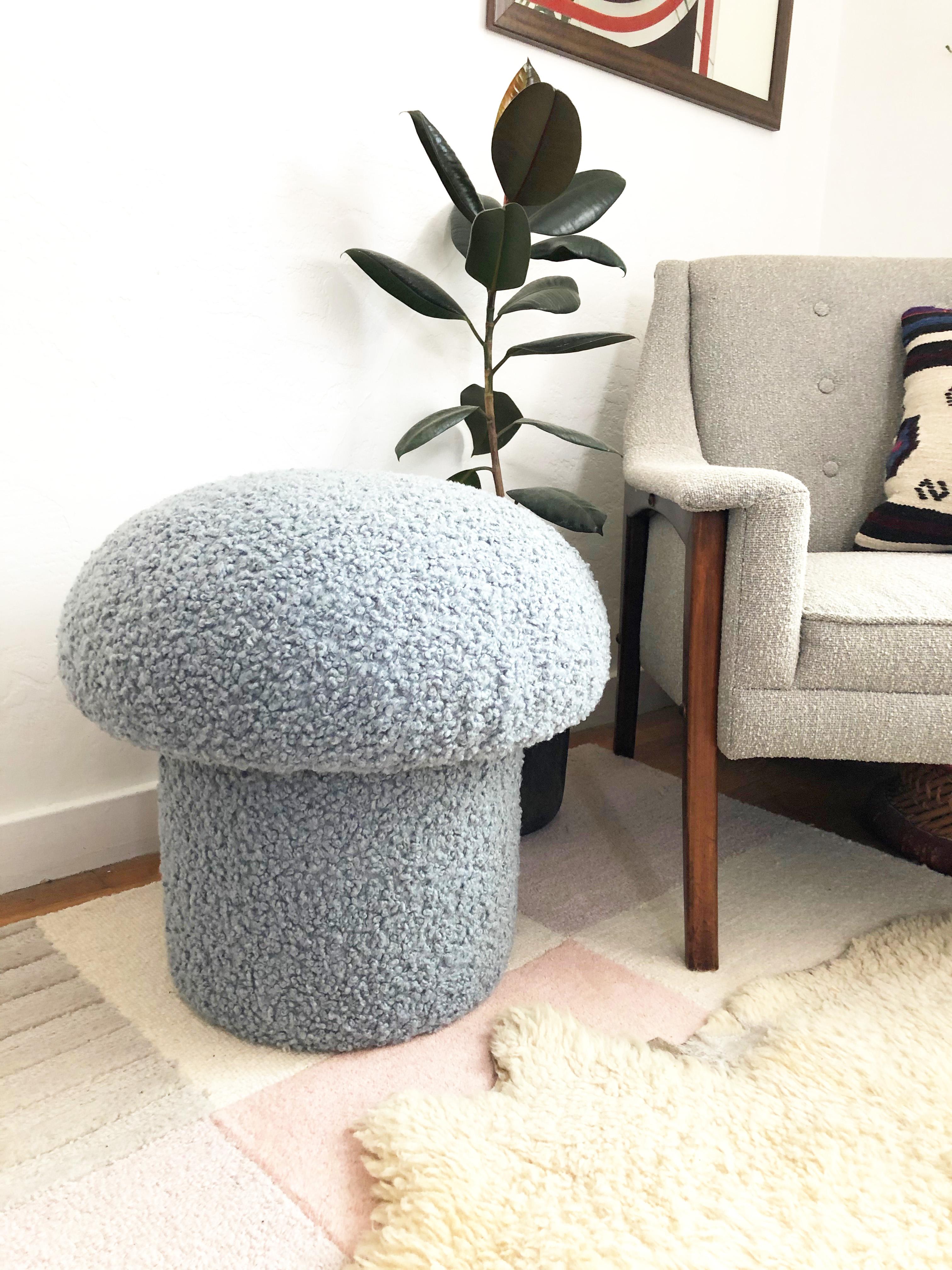 A handmade mushroom shaped ottoman, upholstered in a light blue colored curly boucle fabric. Perfect for using as a footstool or extra occasional seating. A comfortable cushioned seat and sculptural accent piece.
