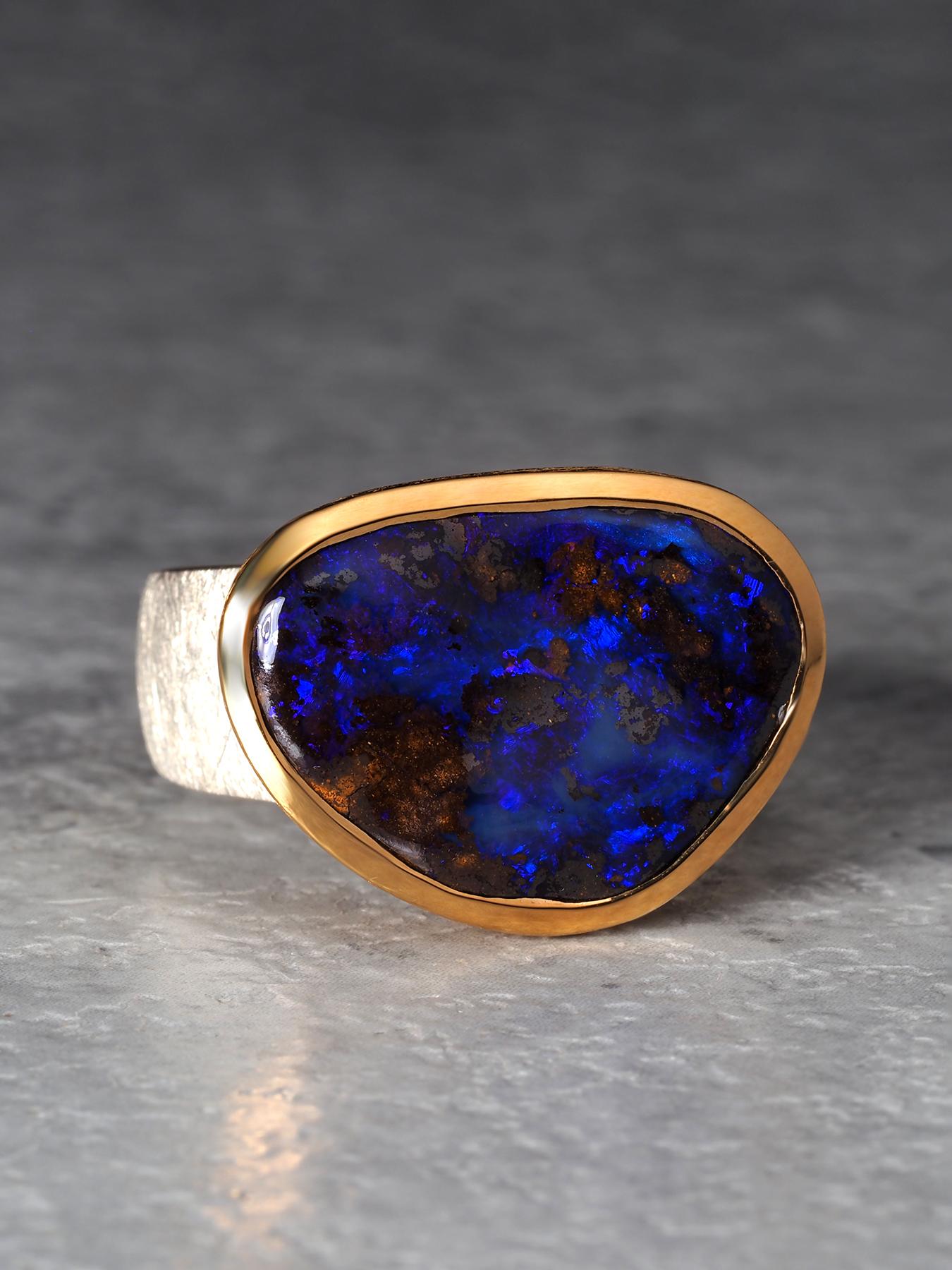 Ein Unisex-Ring mit einem natürlichen australischen Boulder-Opal von beeindruckender Größe, 14 × 19 mm (0,55 × 0,75 Zoll). Der Stein offenbart ein reiches Wechselspiel von tiefblauen und violetten Farbtönen. Sein Farbfeld lebt von subtilen