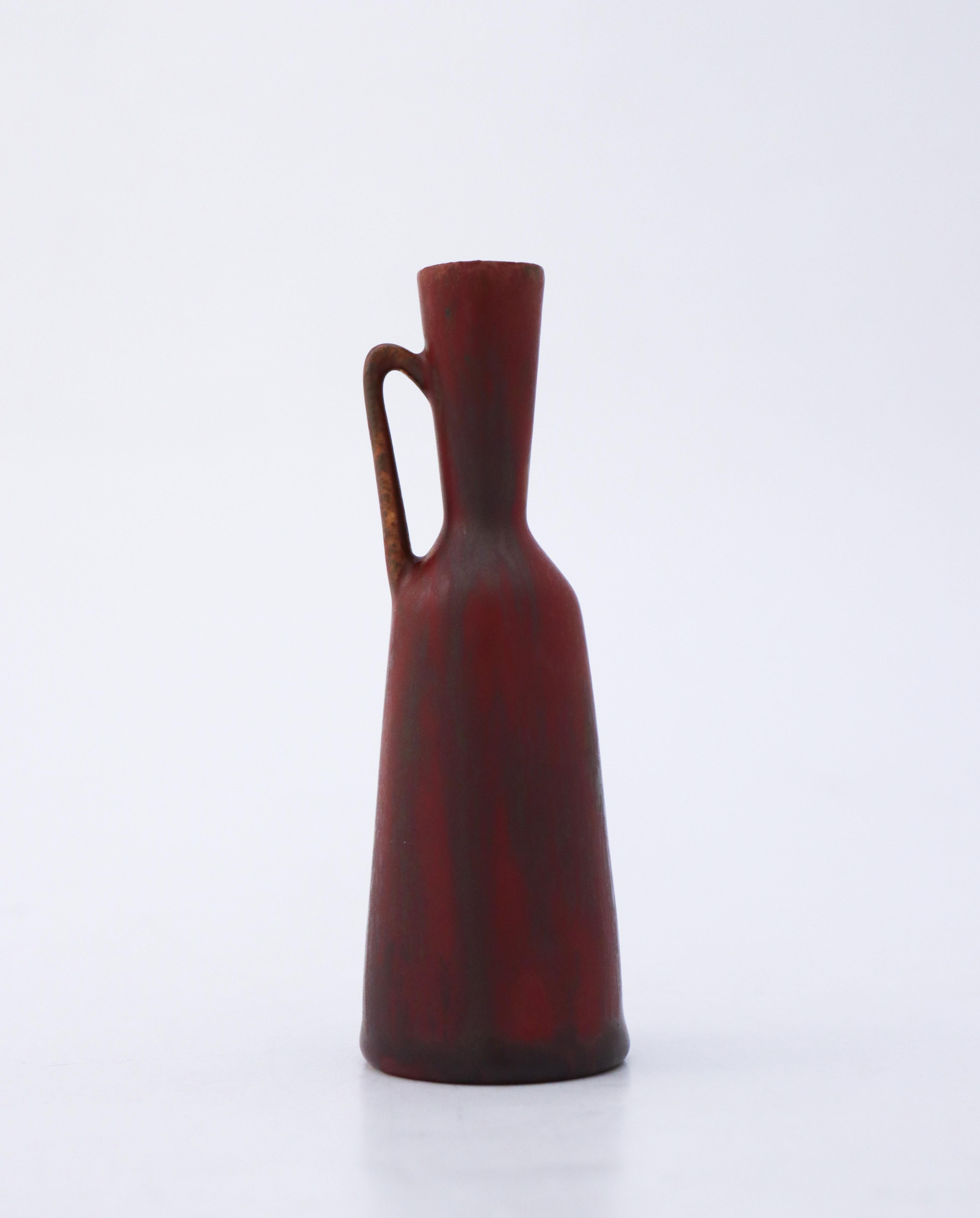 Vase brun/rouge bordeaux conçu par Carl-Harry Stålhane chez Rörstrand, d'une hauteur de 12,5 cm. Il est marqué comme étant de 2ème qualité parce qu'il a une fissure mineure près de la base provenant de la production, voir les photos détaillées de