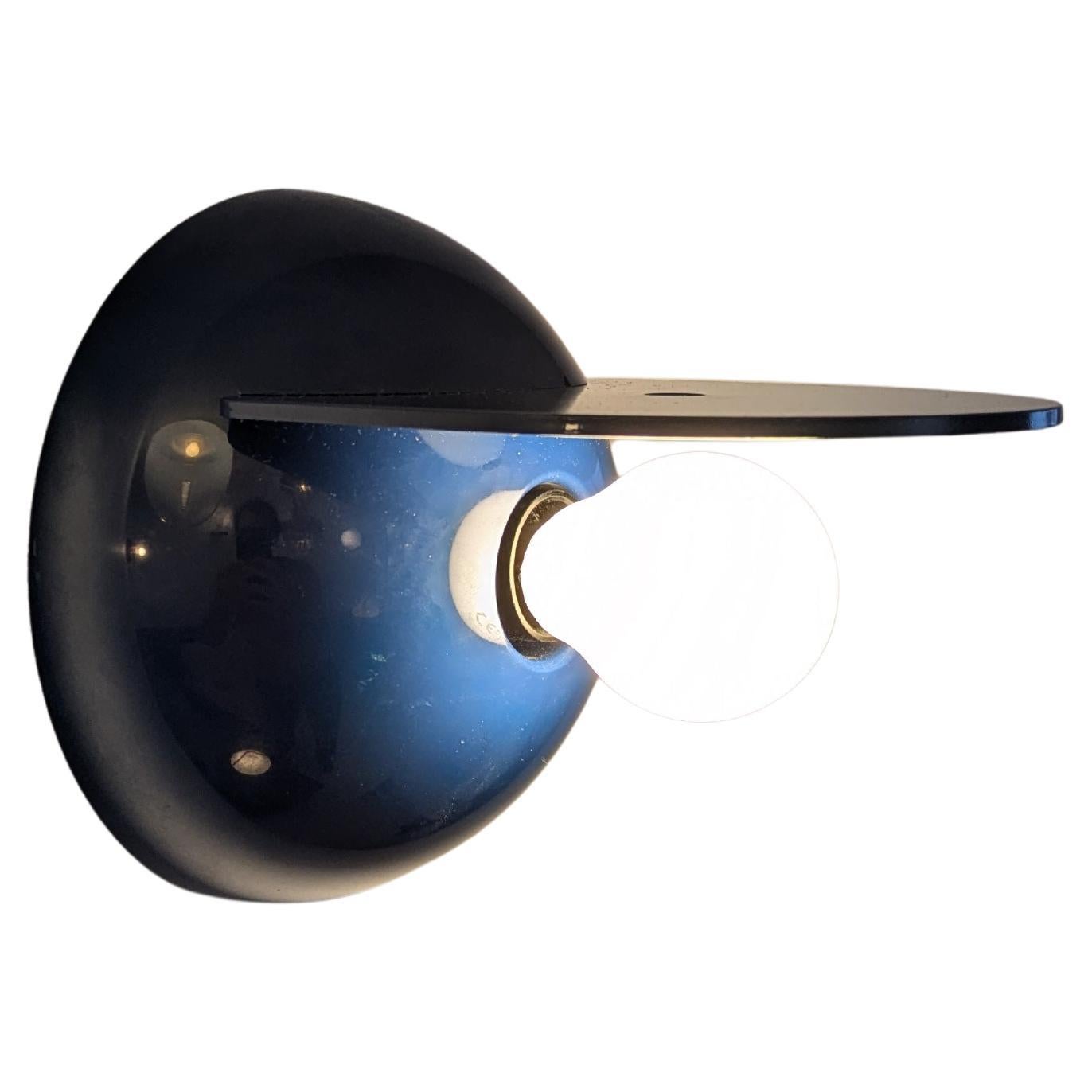 Este aplique Buco (Agujero) es de fabricación italiana y está fabricado por Artemide. Fue diseñada por el diseñador italiano Claudio Dini. 
Es de plástico azul 🔵 (ABS) sobre un soporte de plástico negro que permite que la pieza azul