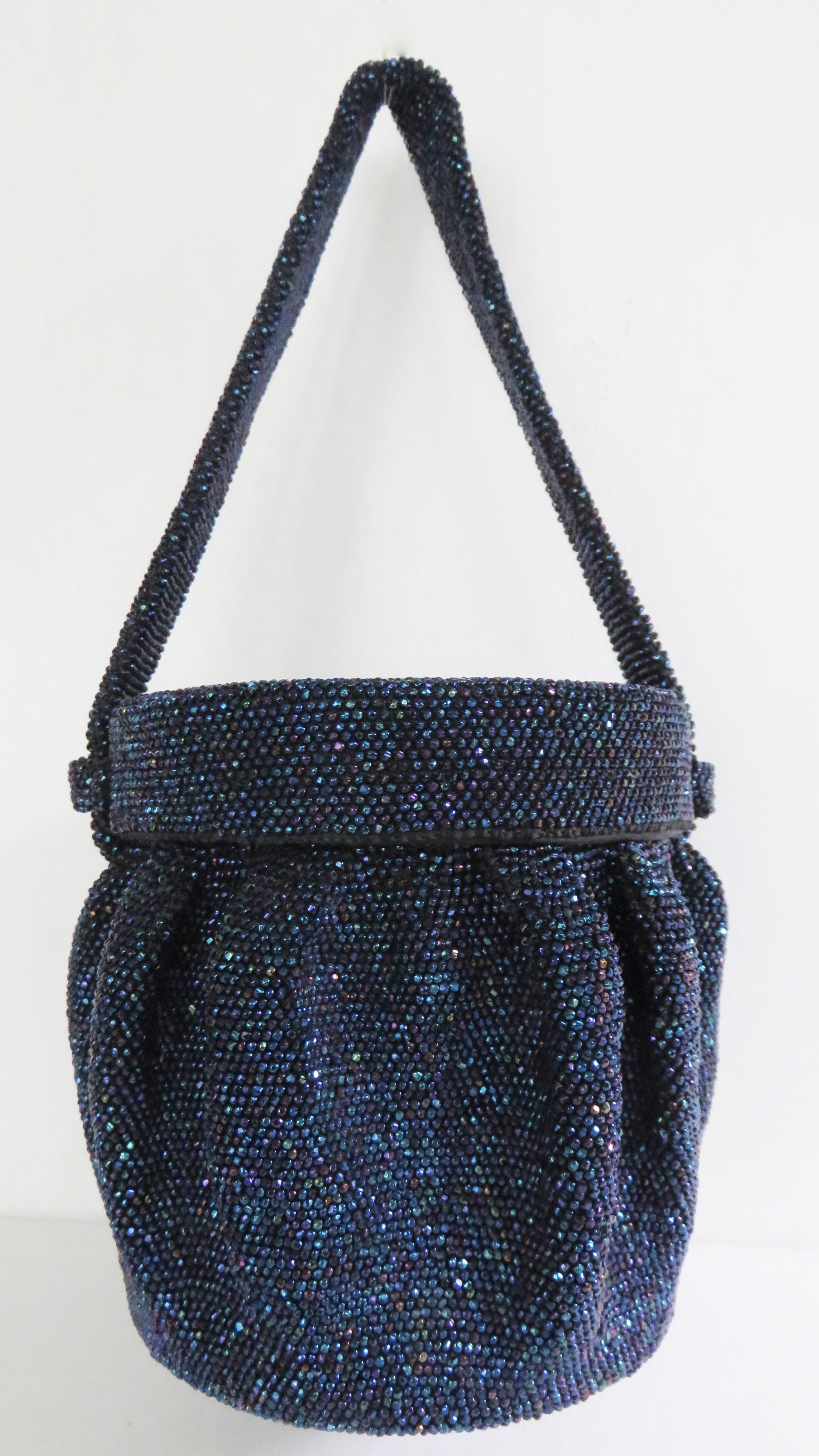 A spectacular midnight blue carnival glass beaded round box purse.  The handbag has vertical raised pleats around it's circumference, a round base and lid which remains attached to the top handle sliding along it to open. It is silk lined and has an