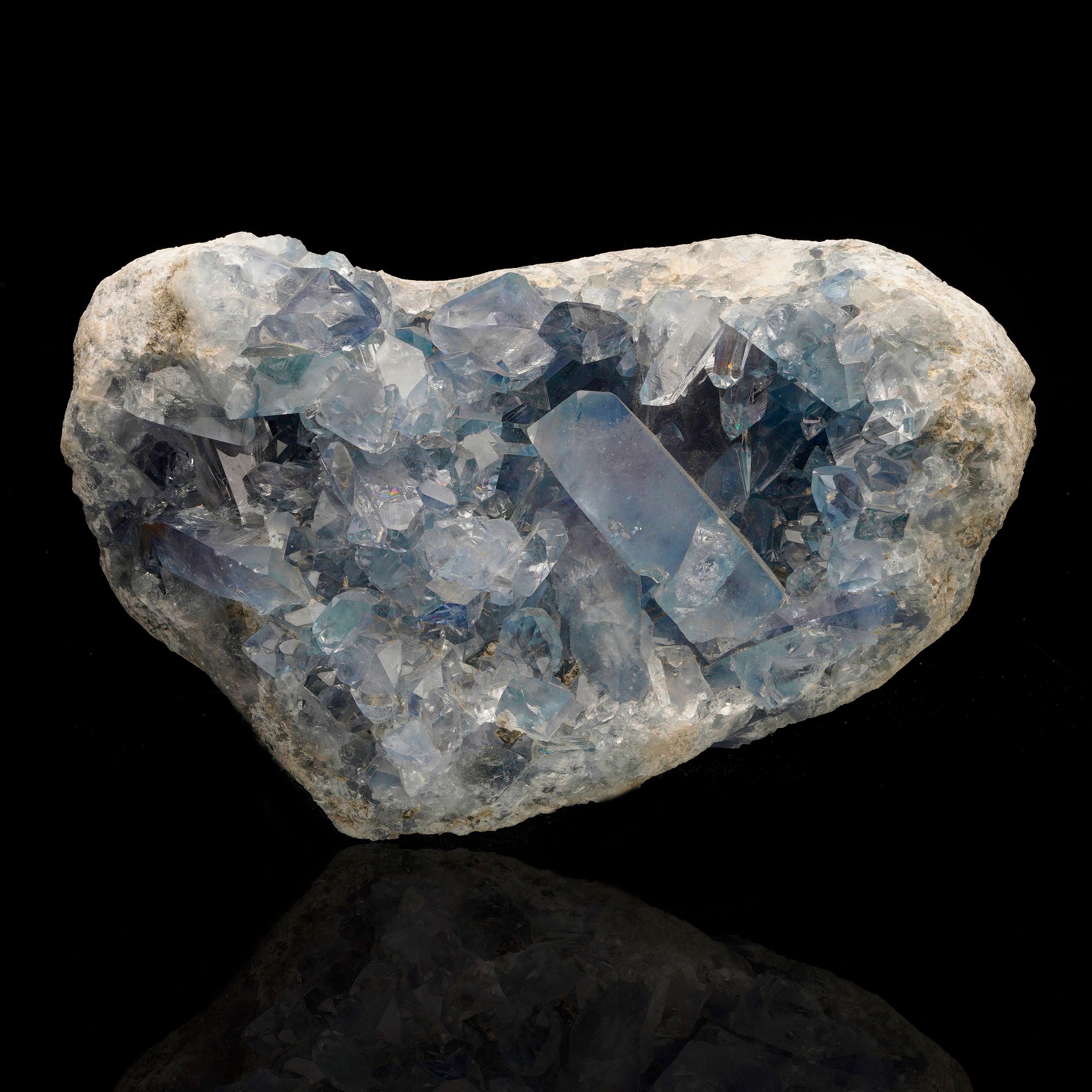 This open blue celestite geode features large, gemmy, glass-clear crystals with light to denim blue pigmentation, many with sharp, perfect terminations. This piece features incredible luster and the prismatic crystals create a treasure trove of