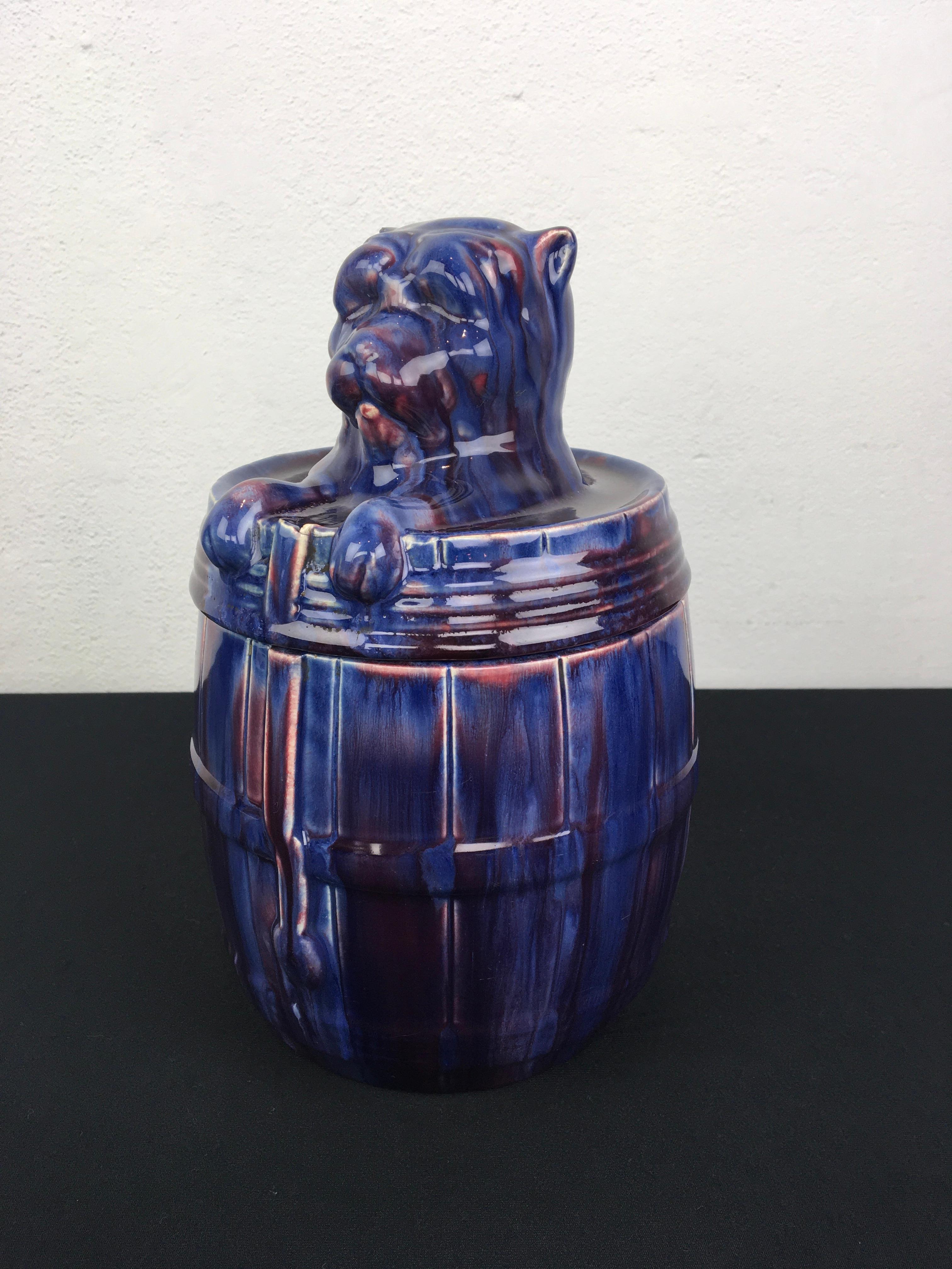 Ceramic bulldog tobacco jar. A dog in a rain barrel numbered 668 - drip glaze ceramic in Art Nouveau style.
A jar with lid in beautiful colors blue and purple. I looks like the dog is sitting in the rain barrel. The type of dog: Bulldog - American