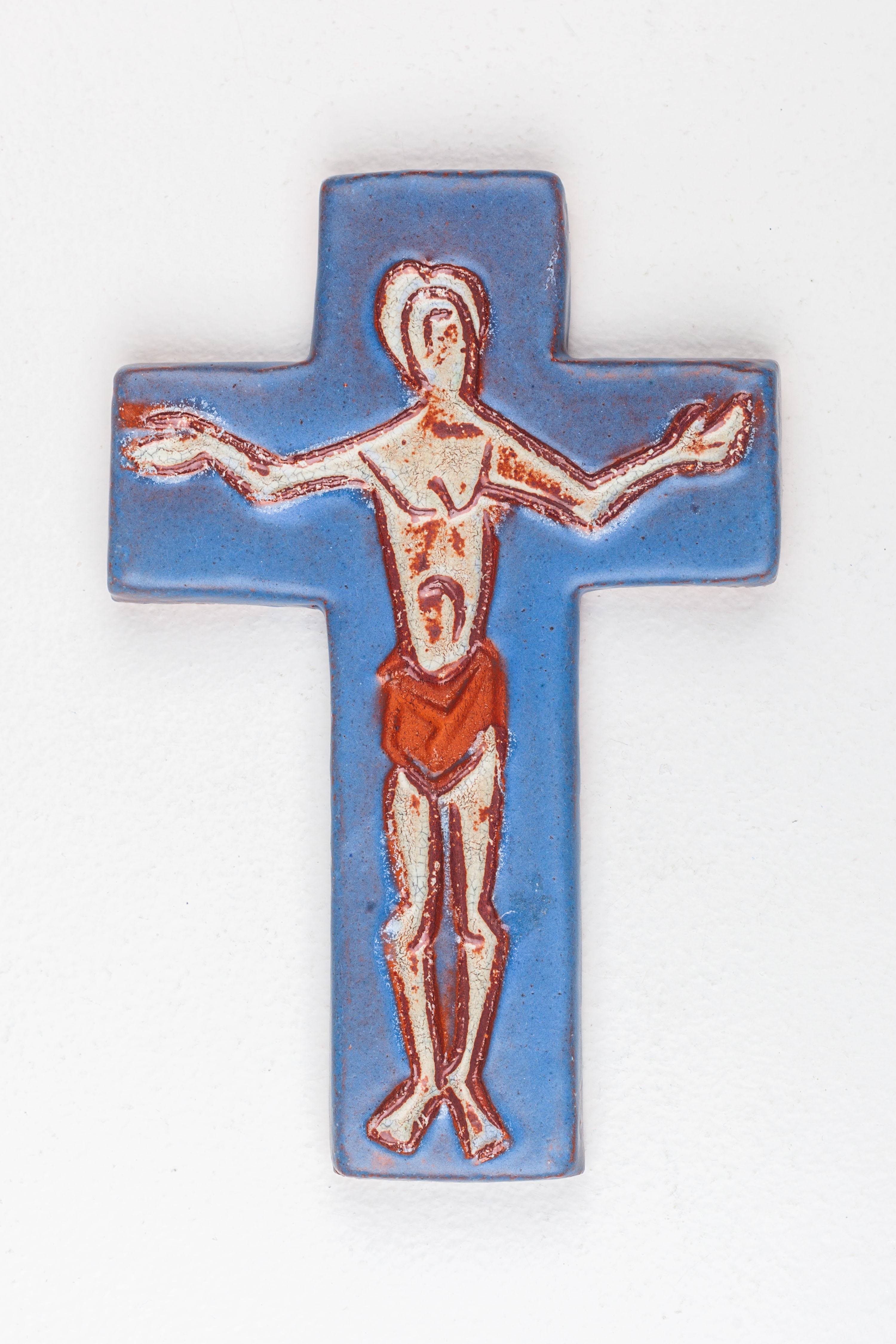 Une croix en céramique bleue avec un Christ abstrait dessiné au trait, enveloppé dans un tissu de couleur rouille. Cette croix fusionne harmonieusement le symbolisme profond de l'iconographie religieuse avec une touche expérimentale, créant ainsi