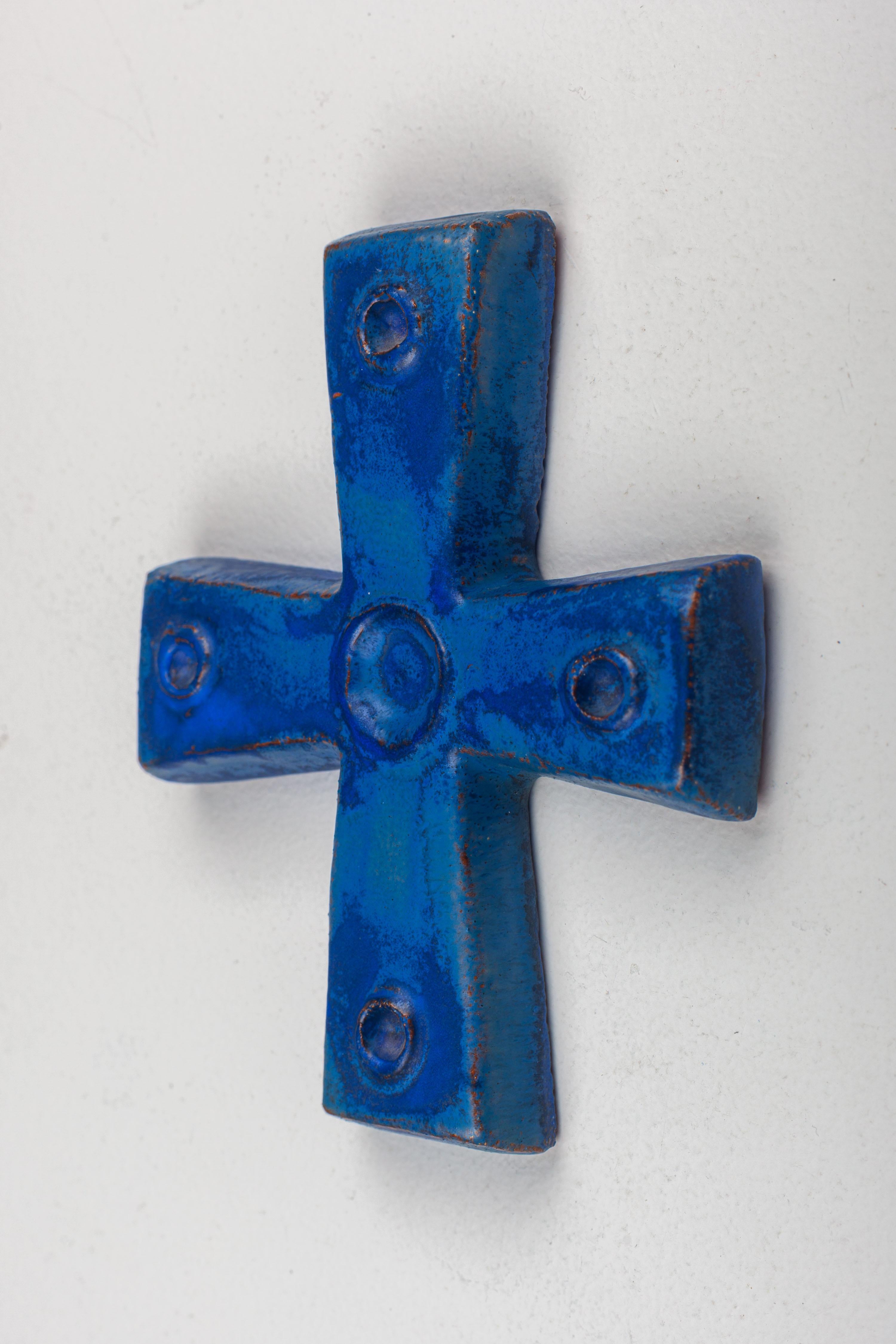 Une croix en céramique du milieu du siècle réalisée par un artisan flamand dans un bleu Klein profond et lumineux. Chaque pointe de la croix et son centre sont ornés d'embellissements circulaires en relief creux, ajoutant des couches d'intrigue