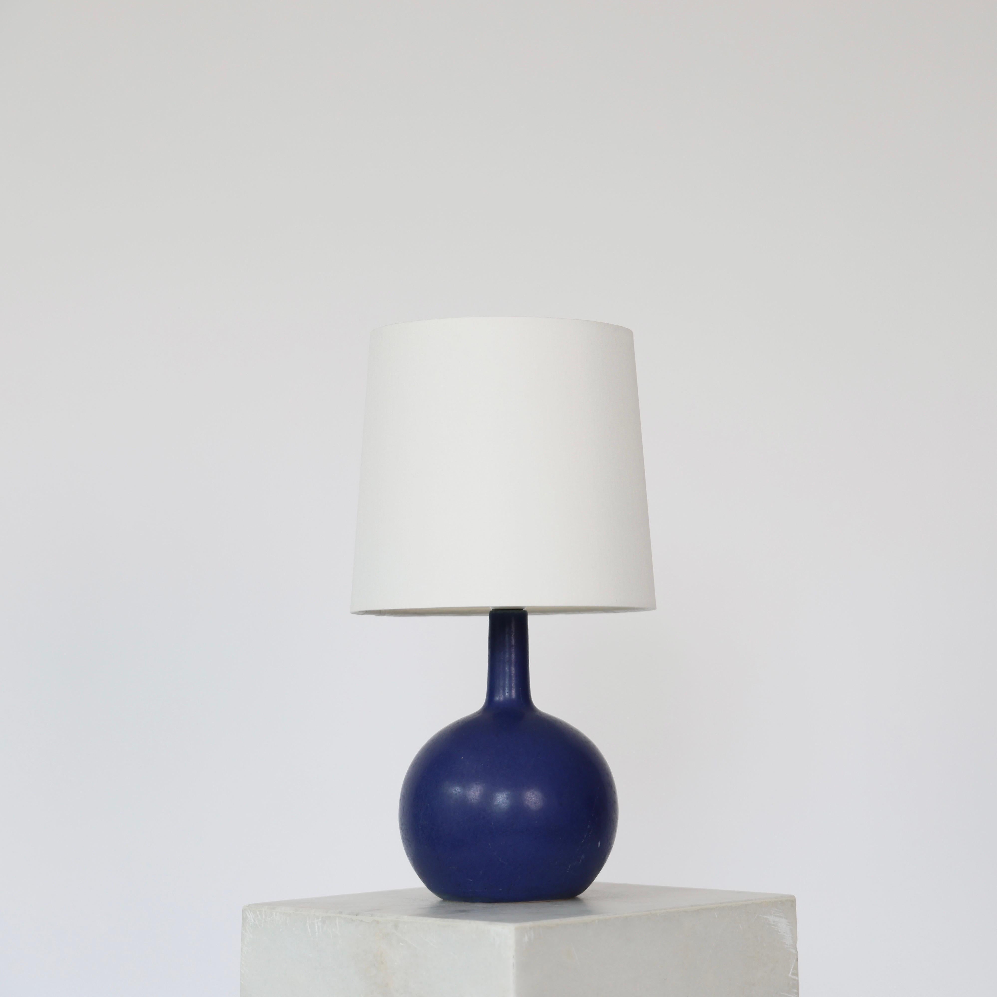 Lampe de table en céramique moderne danoise bleue fabriquée par Eigil Hindrichsen dans les années 1950. 

* Lampe de table ronde en céramique bleue avec un col étroit et un abat-jour en tissu blanc. 
* Designer : Eigil Hindrichsen
* Année : est.