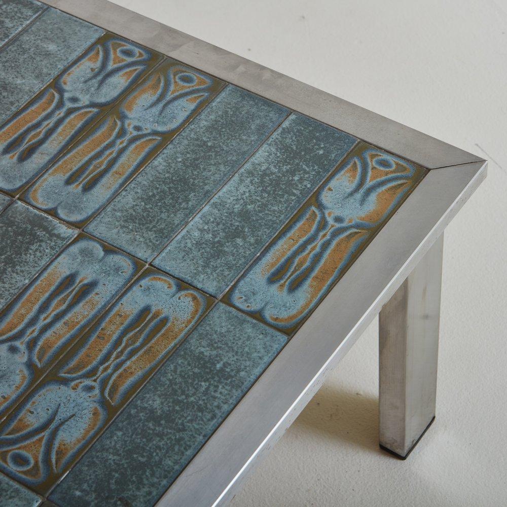 ??A vintage French coffee table featuring a beautiful glazed ceramic tile top with rich color variations in blue, gray and taupe hues. Several of the rectangular tiles have a beautiful abstract pattern. The tabletop is set within an angular chrome