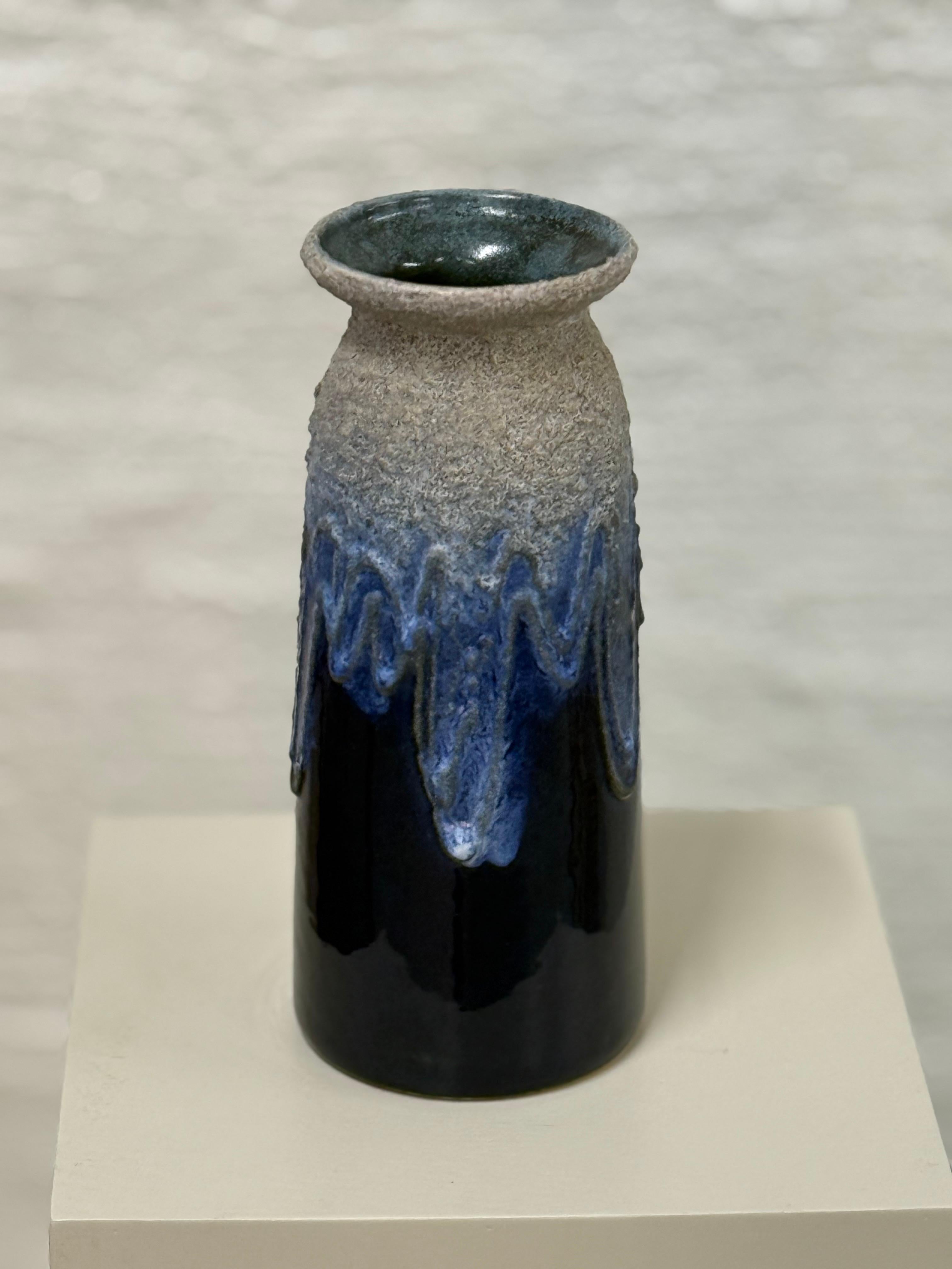 Este llamativo jarrón de cerámica fue fabricado por Strehla Keramik, un conocido fabricante de cerámica de la ciudad de Strehla, en la antigua Alemania Oriental (RDA). Strehla era conocida por sus atrevidos esmaltes, sus superficies texturadas y su