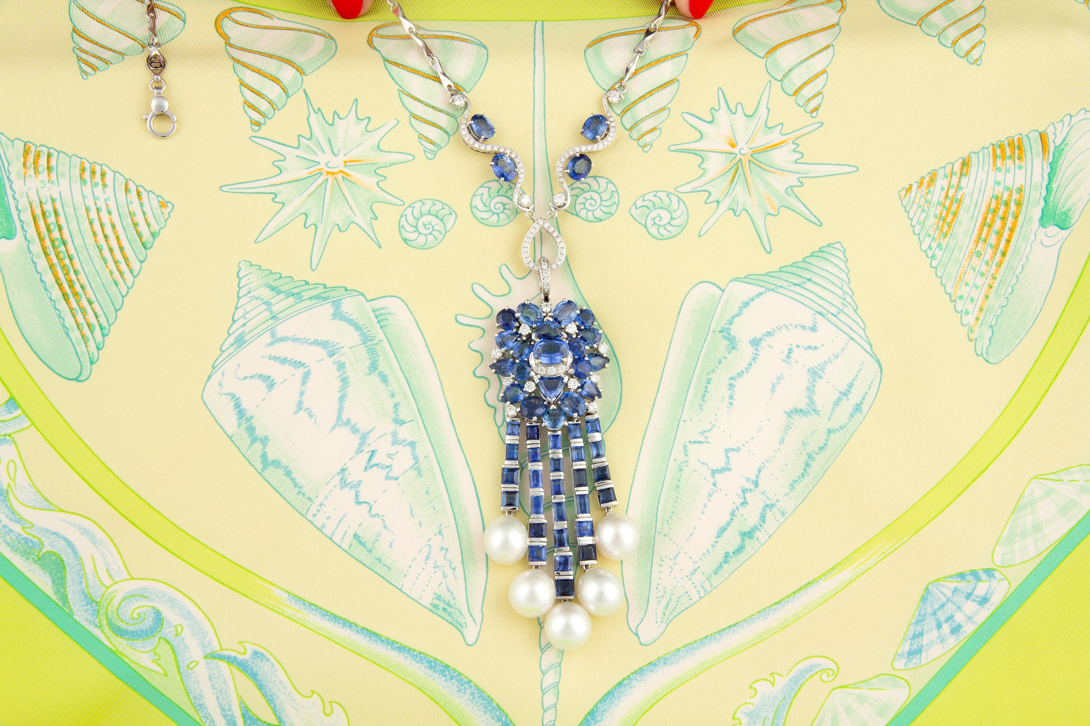 The blue sapphire and diamond pendant features a floral cluster of drop and oval shape Ceylon sapphires spangled with diamonds and suspending an articulated cascade of custom cut blue sapphire baguettes. The design is complete with 5 South Sea