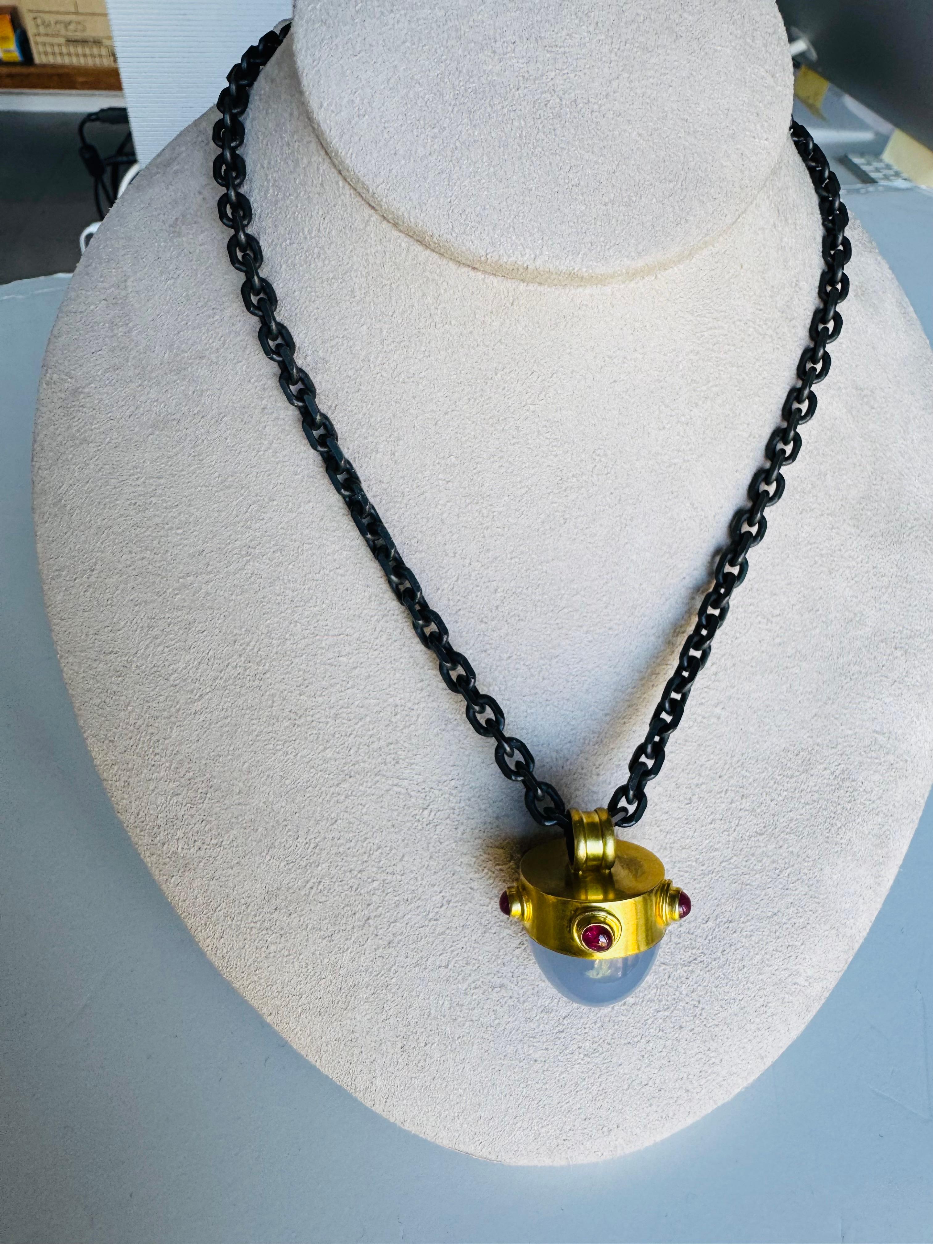 Ispirato alle forme audaci dei gioielli medievali, questo sostanzioso calcedonio blu a forma di proiettile - del peso di ben 50 carati - è incastonato in un ricco oro a 22 carati e circondato da cabochon di rubini luminosi. La sua presenza imponente