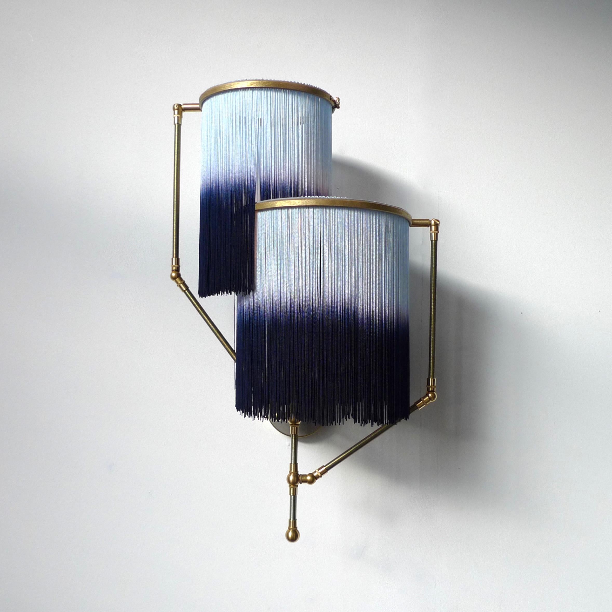 Blue Charme sconce lamp, Sander Bottinga

Dimensions: 50 x W 38 x D 27 cm.
Hand-sculpted in brass, leather, wood and dip dyed colored Fringes in viscose.
The movable arms makes it possible to move the circles with fringes in differed