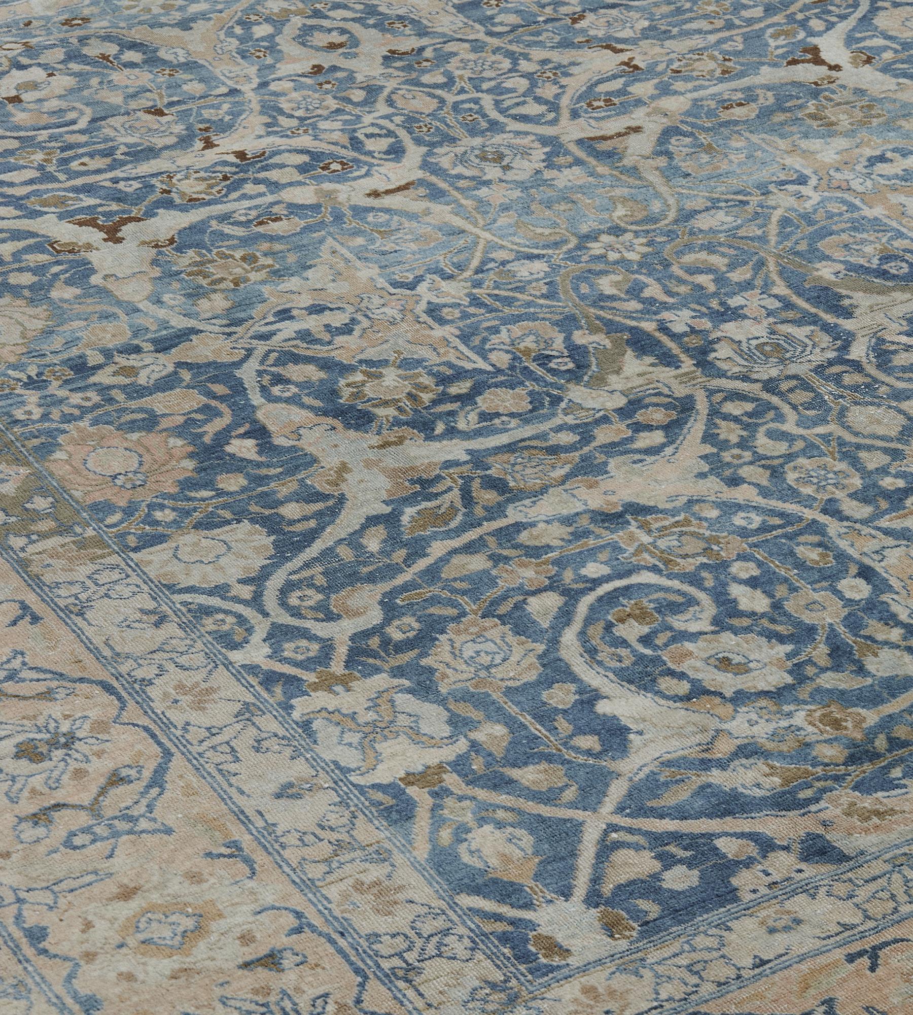 Ce tapis ancien de Tabriz, datant d'environ 1910, présente un champ bleu nuancé avec un motif d'ensemble de vigne à feuilles d'acanthe fendues brun sable et bleu clair émettant une variété de têtes de fleurs et de vrilles feuillues, une colonne de