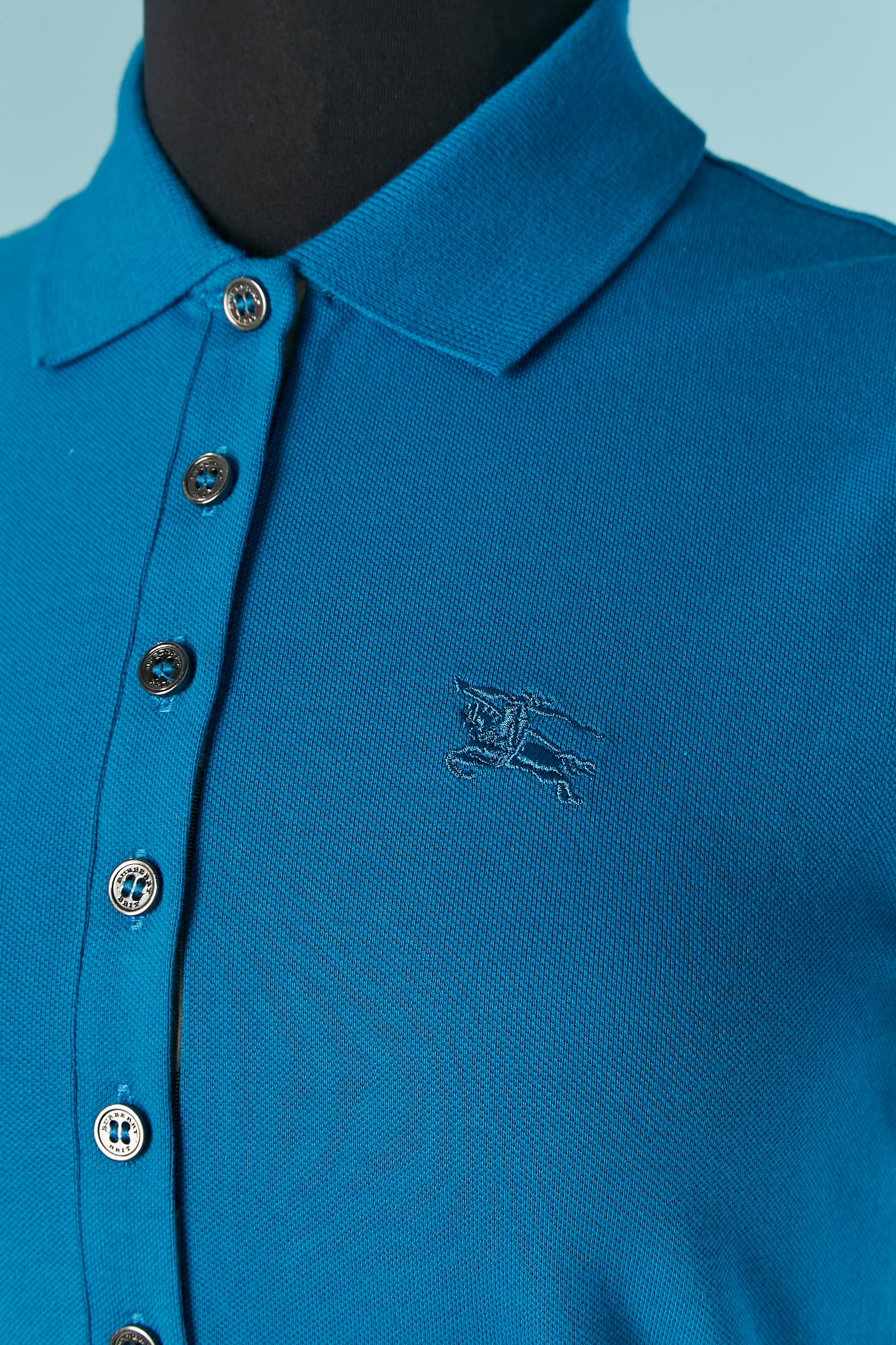 Polo en coton bleu. Bouton et boutonnière marqués sur le haut du devant. Vérifier le tissu à l'intérieur de l'ouverture du bouton. Un bouton supplémentaire est fourni.
Composition du tissu : 98% coton, 2% élasthanne. 
TAILLE XS 