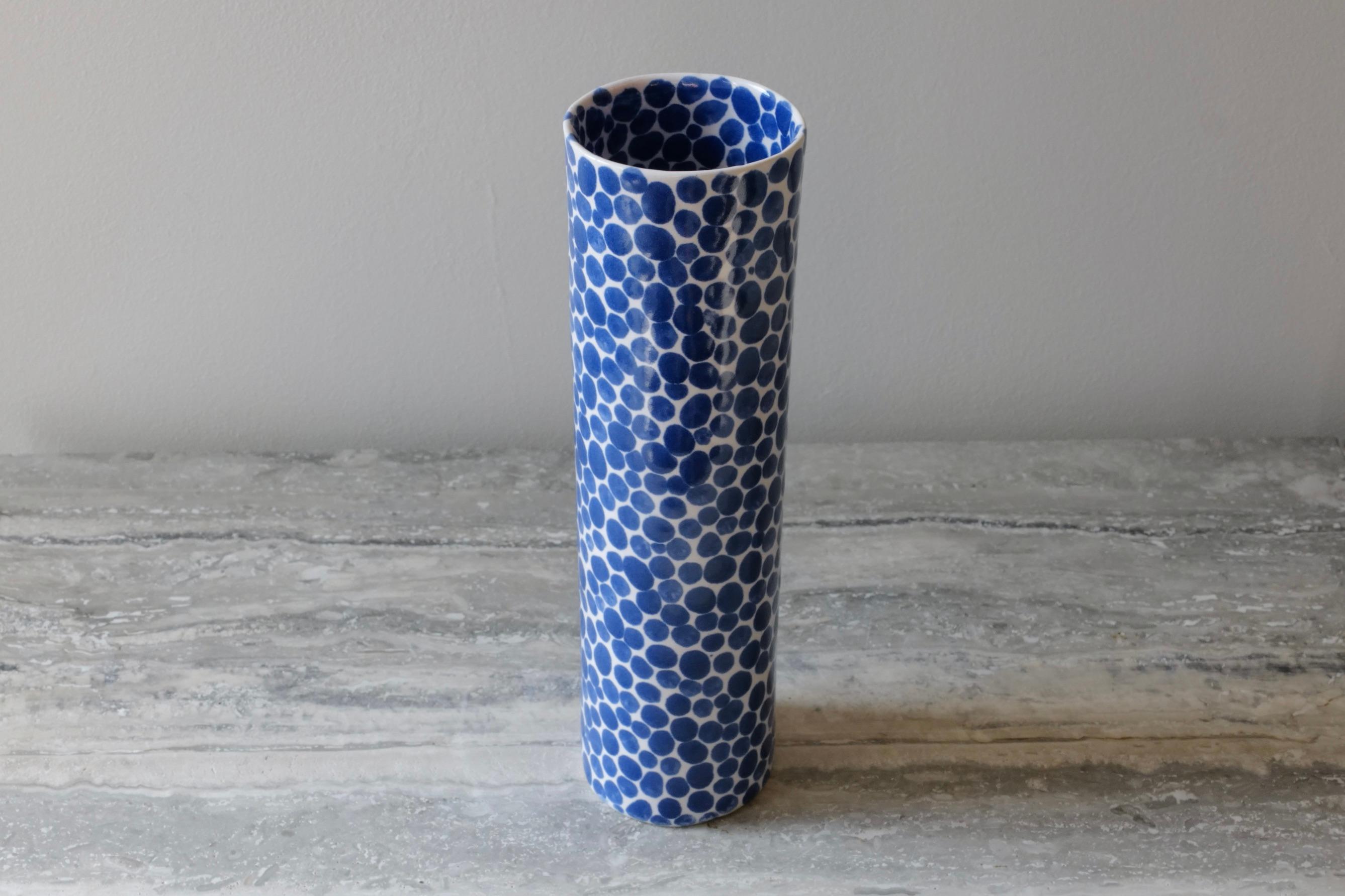 Tall, thin and elegant ceramic vase. Hand-cast in porcelain and once bisque fired, each dot is hand-painted with a traditional cobalt blue glaze. An unconventional layered glazing technique, developed by the artist, is used in these cast porcelain