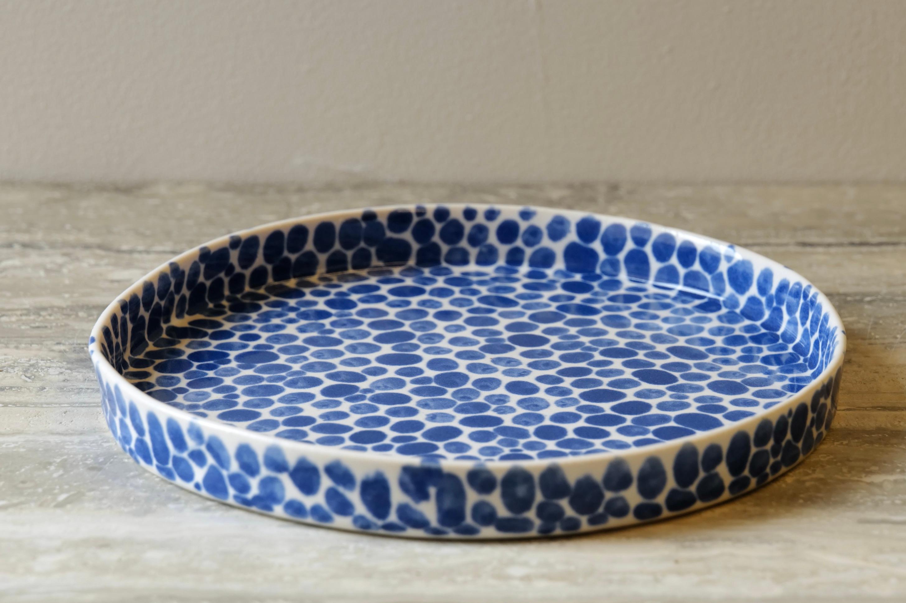 Small porcelain plate. Hand-cast in porcelain and once bisque fired, each dot is hand-painted with a traditional cobalt blue glaze. An unconventional layered glazing technique, developed by the artist, is used in these cast porcelain pieces. The