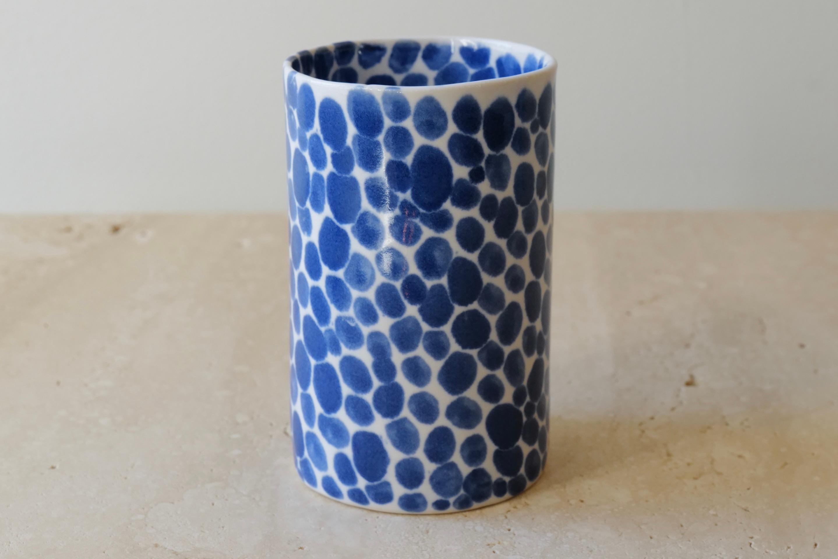 Ceramic drinking cup. Hand-cast in porcelain and once bisque fired, each dot is hand-painted with a traditional cobalt blue glaze. An unconventional layered glazing technique, developed by the artist, is used in these cast porcelain pieces. The