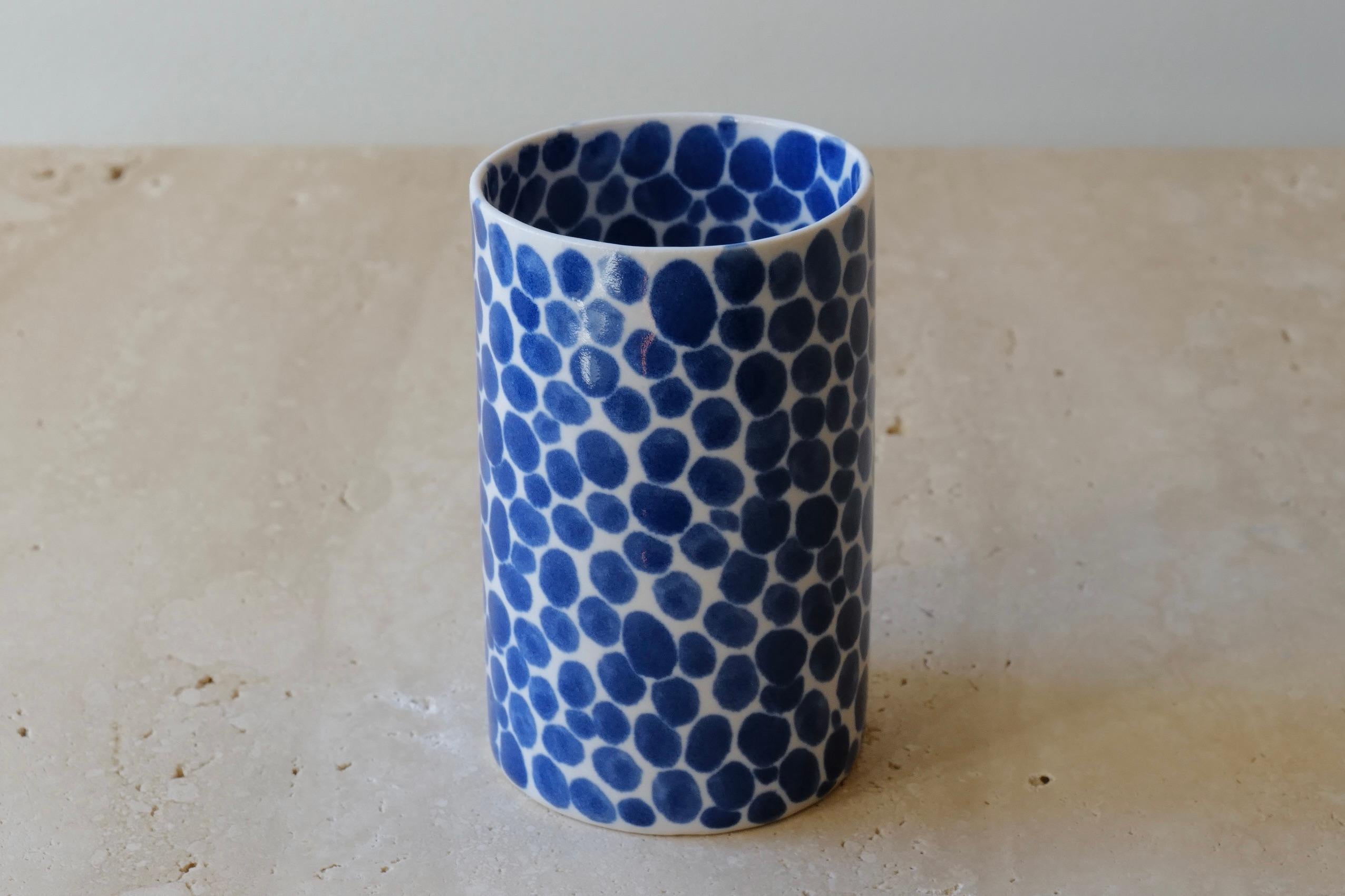 Ceramic drinking cup. Hand-cast in porcelain and once bisque fired, each dot is hand-painted with a traditional cobalt blue glaze. An unconventional layered glazing technique, developed by the artist, is used in these cast porcelain pieces. The