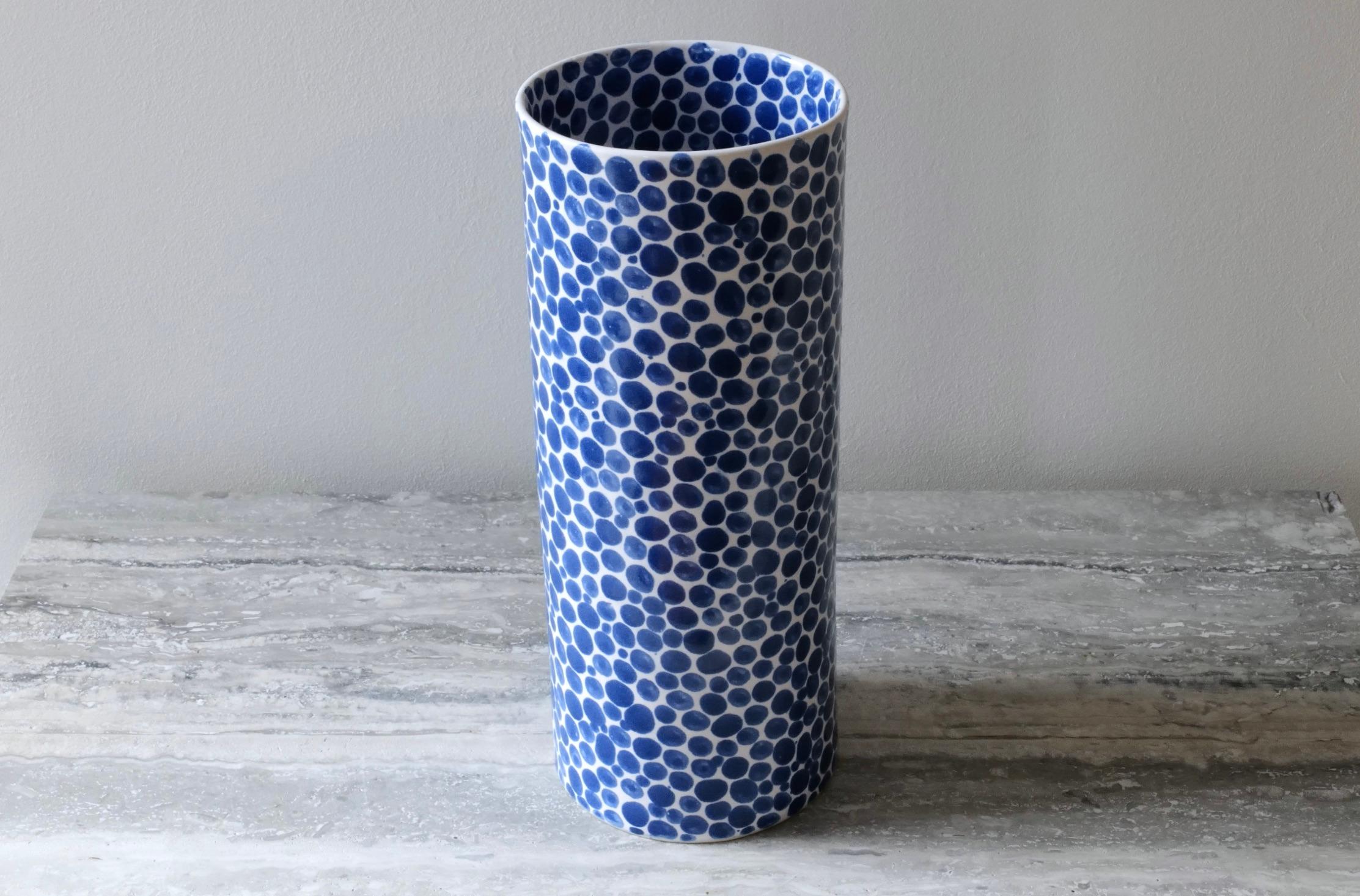 Large, tall ceramic vase. Hand-cast in porcelain and once bisque fired, each dot is hand-painted with a traditional cobalt blue glaze. An unconventional layered glazing technique, developed by the artist, is used in these cast porcelain pieces. The