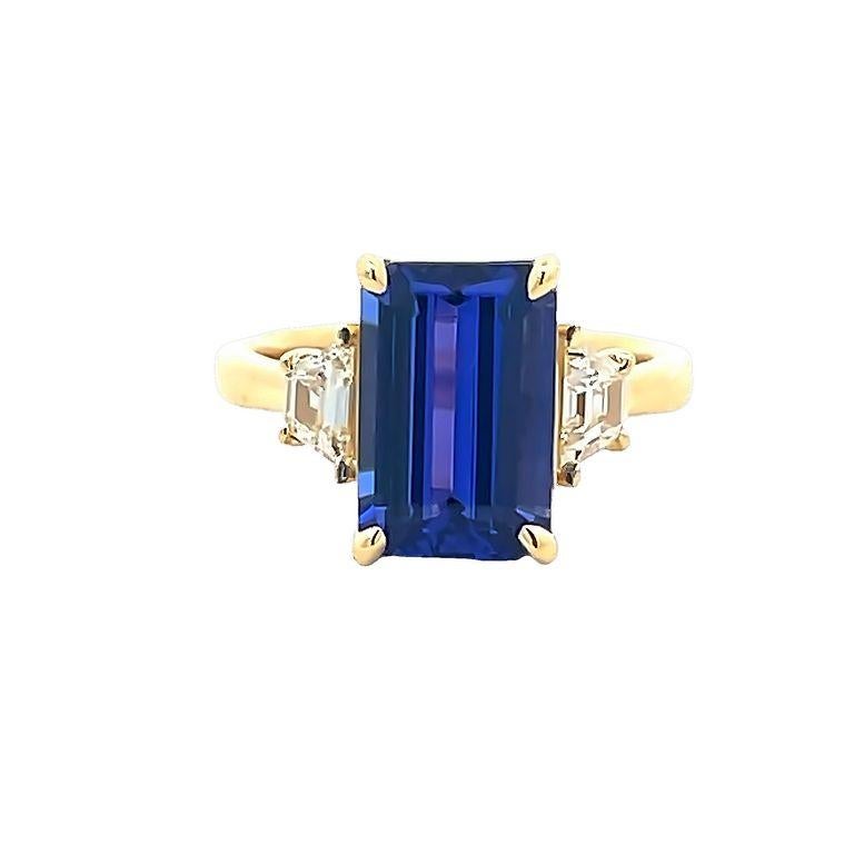 Be prepared to be amazed by the breathtaking beauty of this three-stone ring. The centerpiece features a stunning emerald-shaped blue tanzanite, considered the finest color for this gemstone. The ring's center stone weighs 4.40 carats and is flanked