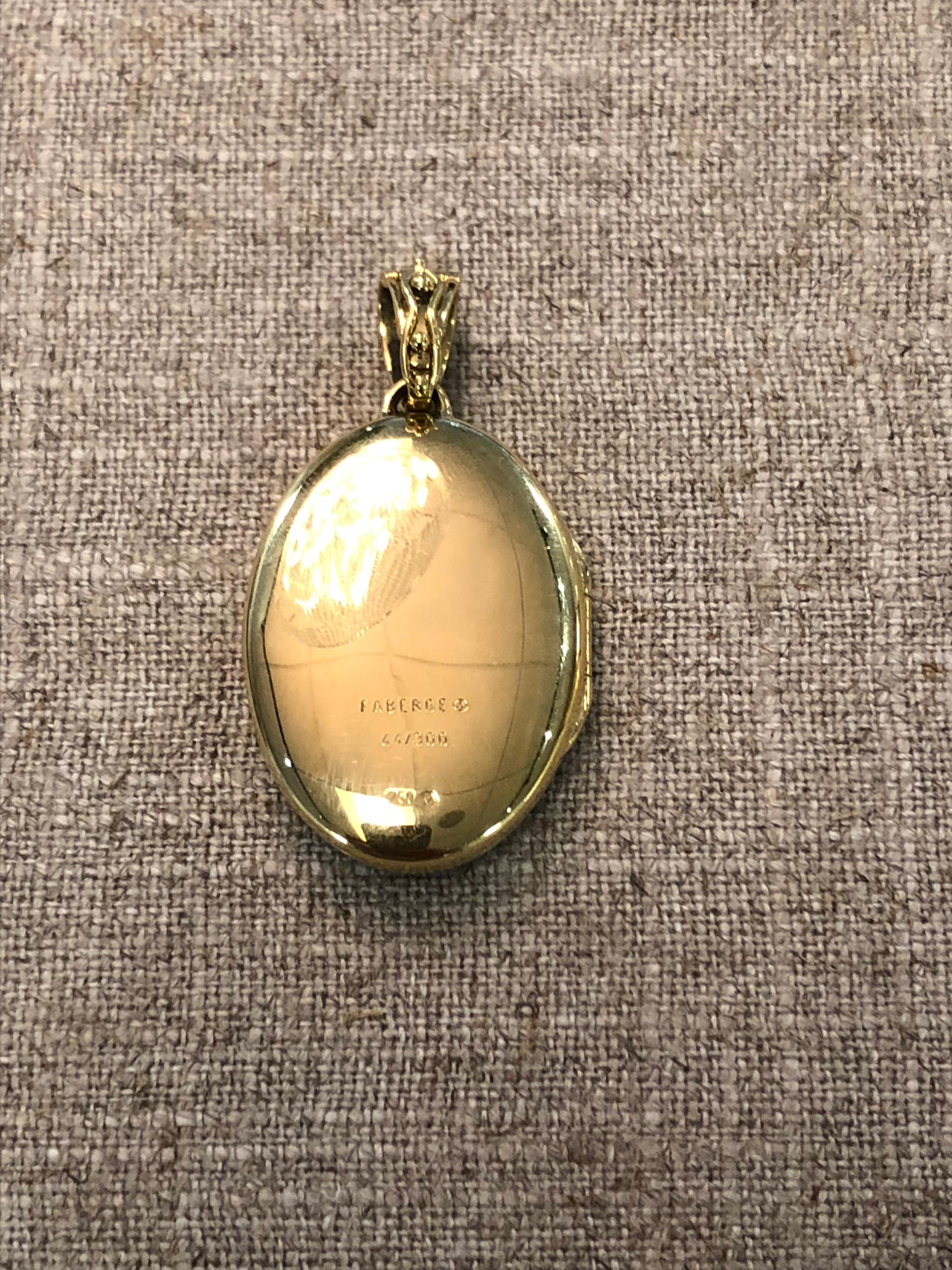 18 karat yellow gold faberge oval locket. The locket features blue enamel with gold floral detailing and pave set diamonds on the bail weighing .04 carats. with original certificate. It is 2