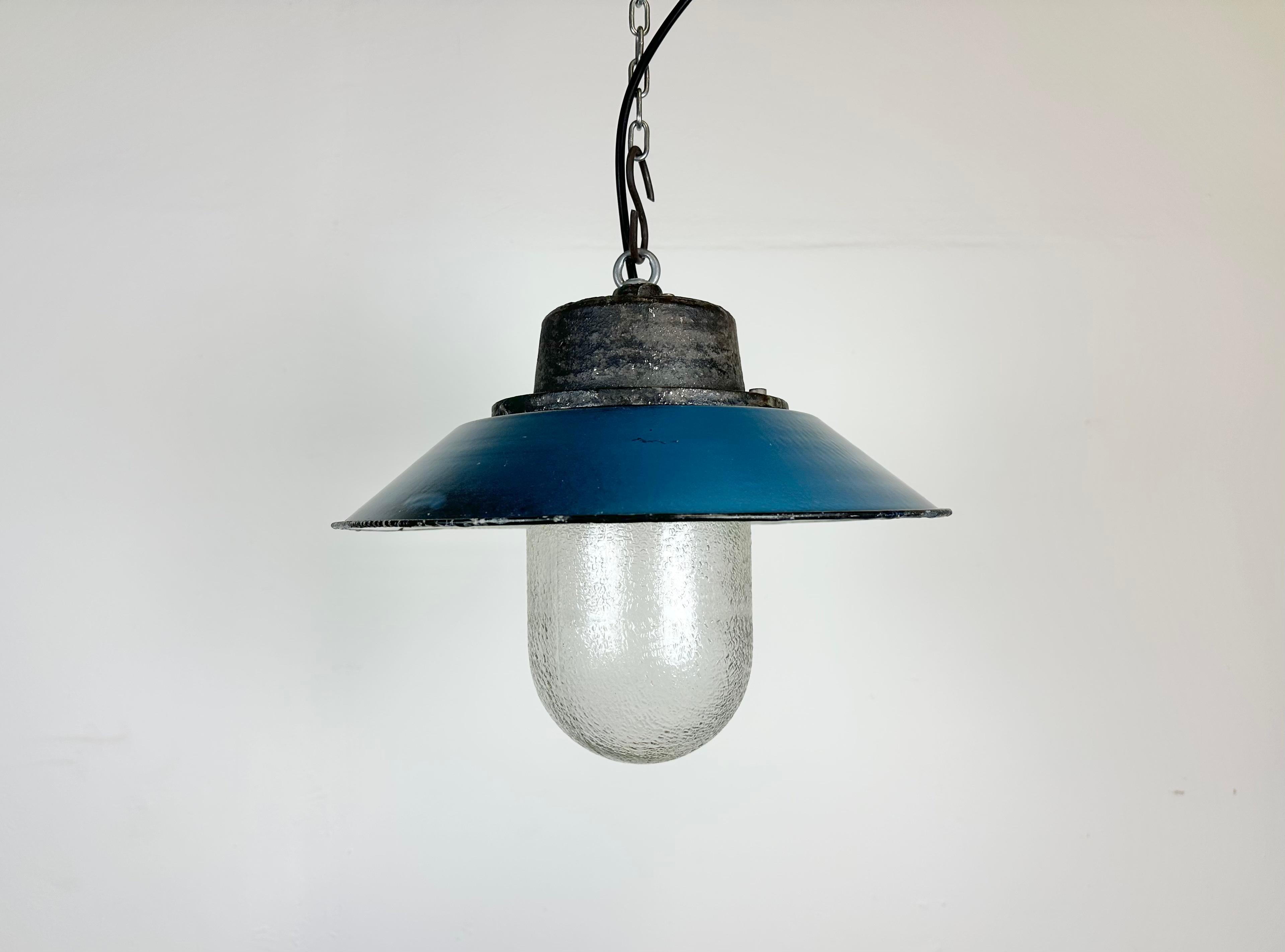 Industrial hanging lamp manufactured in Poland during the 1960s. It features a blue enamel shade with white enamel interior, a cast iron top and a frosted glass cover. The porcelain socket requires E 27/ E26 lightbulbs .New wire. The weight of the