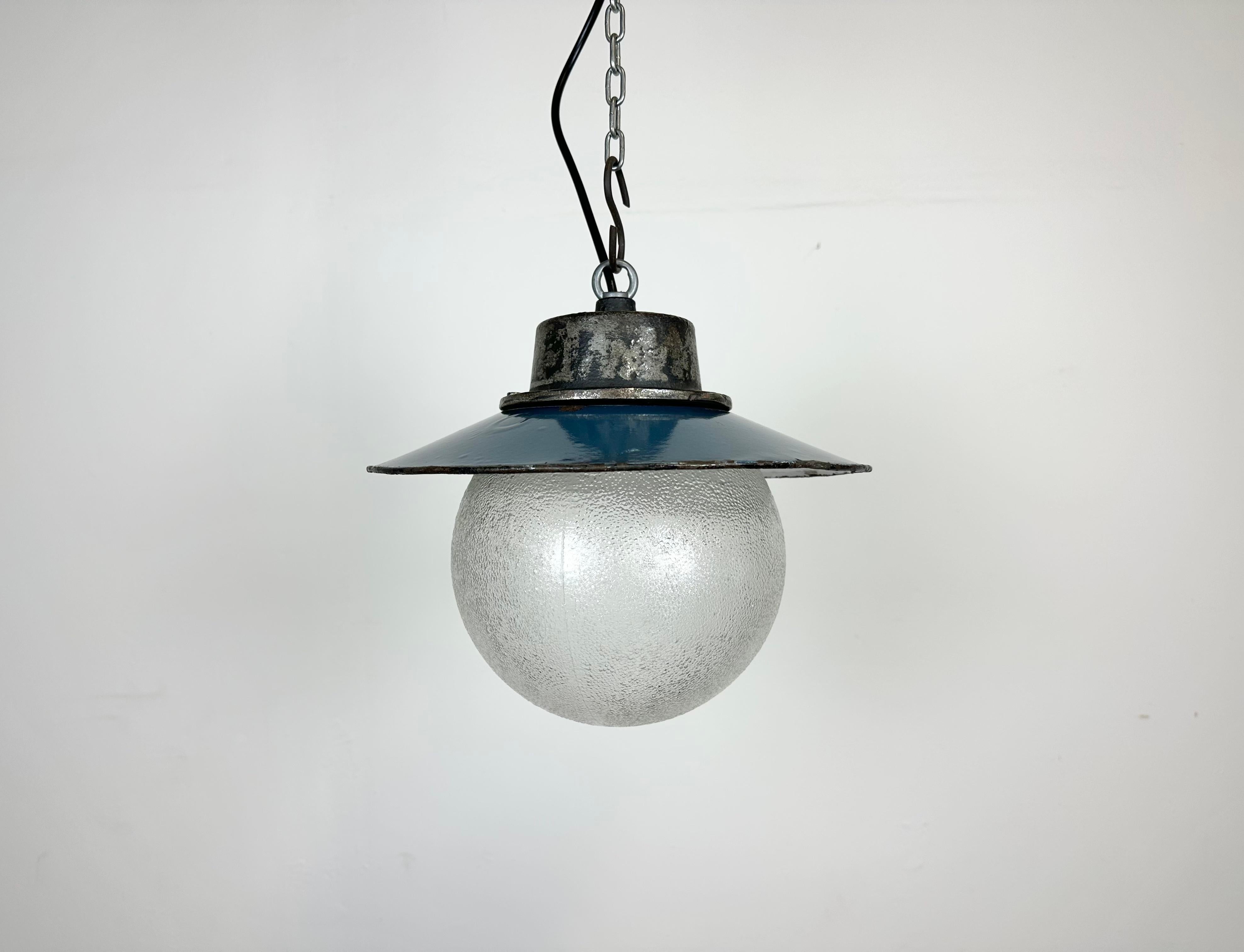 Industrial hanging lamp manufactured in Poland during the 1960s. It features a blue enamel shade with a white enamel interior, a cast iron top, and a frosted glass cover. The porcelain socket requires E 27/ E26 lightbulbs. New wire. The weight of