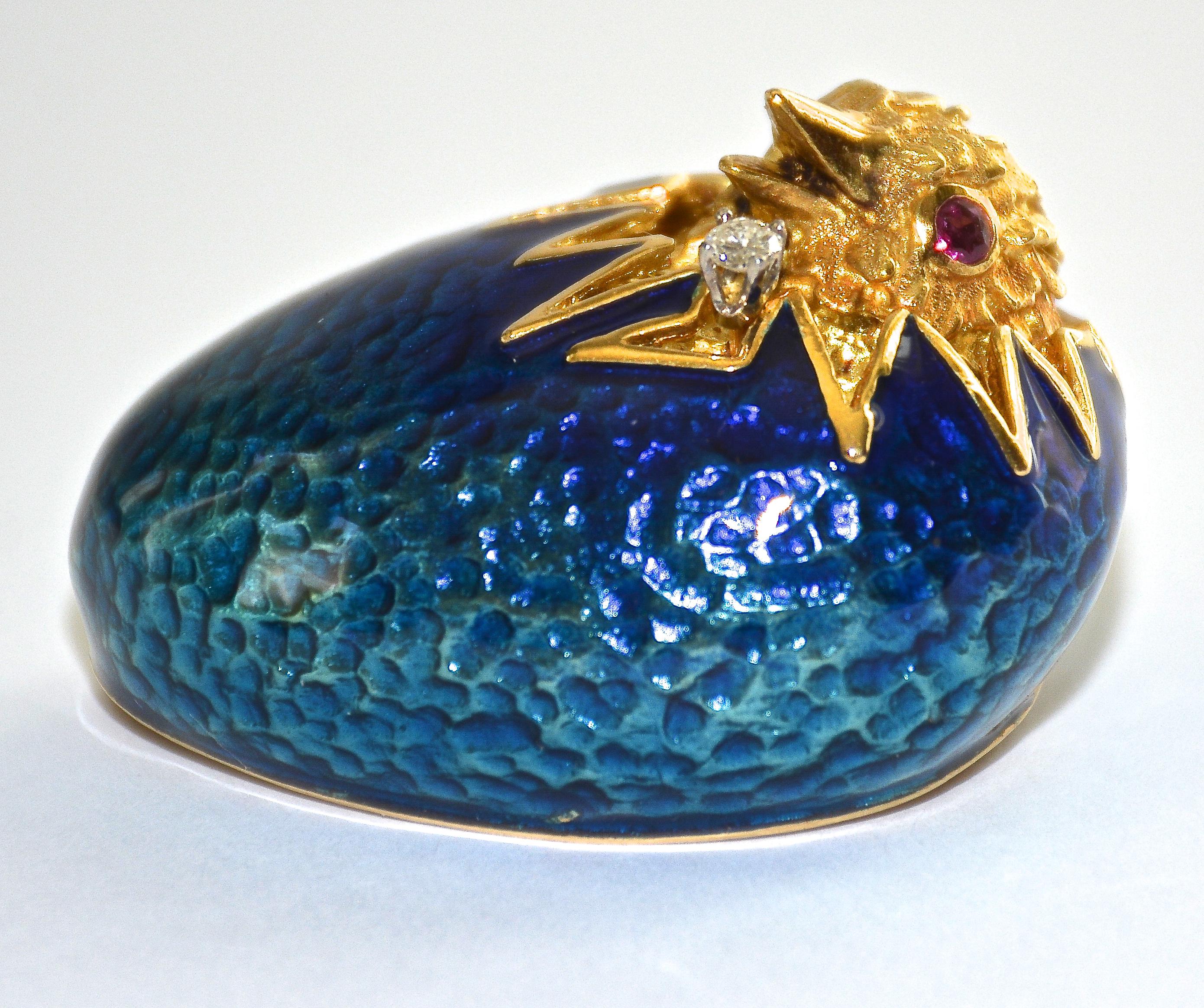 Cette magnifique broche représente un œuf émaillé bleu avec un poussin en train d'éclore.

Serti d'un diamant taille brillant pesant environ 0,05 carat, de couleur H-I et de pureté VS. Les yeux sont rehaussés de deux rubis ronds.

 Le revers