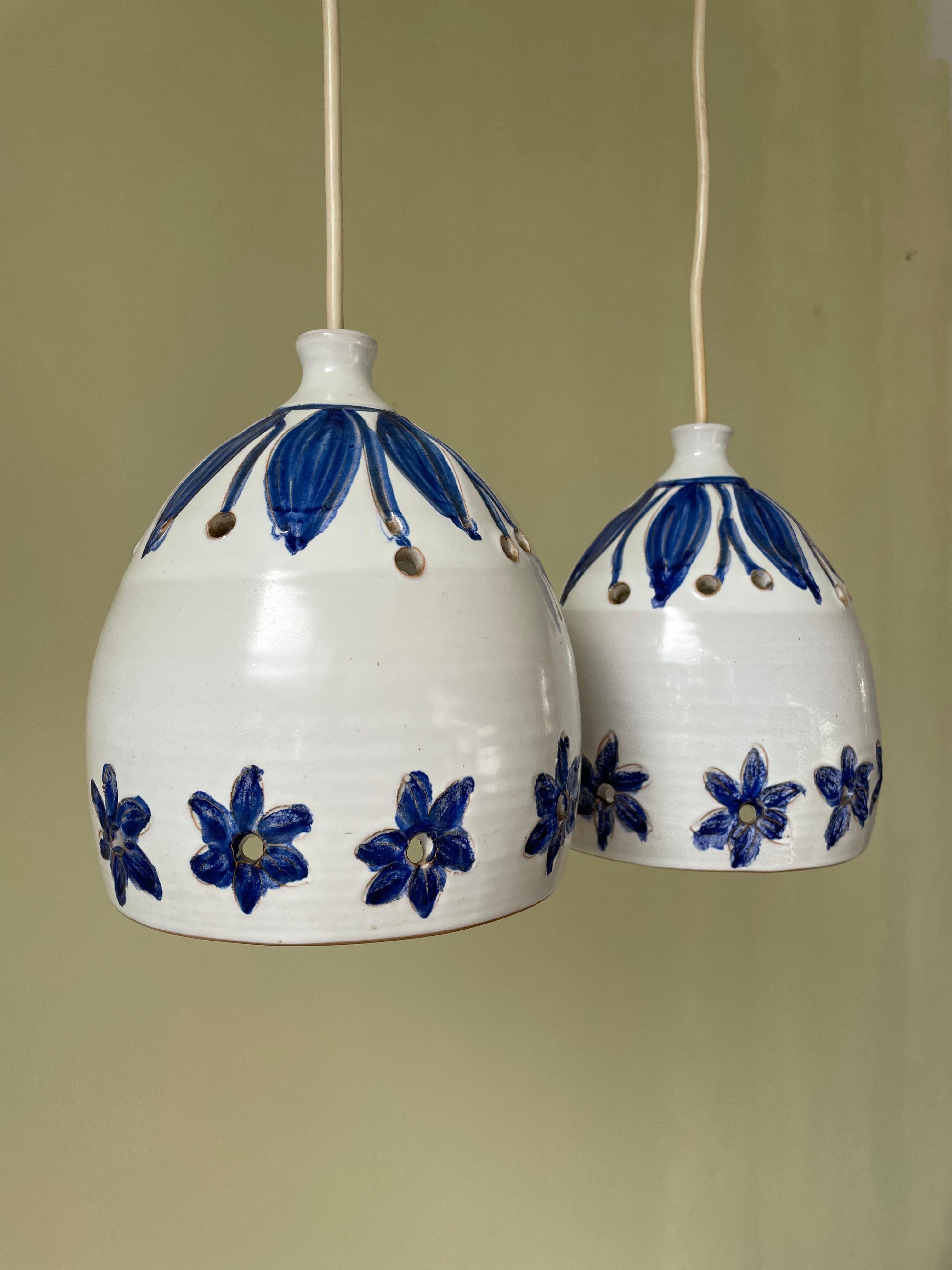 Set of two handmade organic midcentury modern ceramic pendants glazed white with hand-carved and hand-painted blue flowers and leaves. Circular perforations along the top and bottom to let the light out. Shiny white glaze on the inside, raw bottom