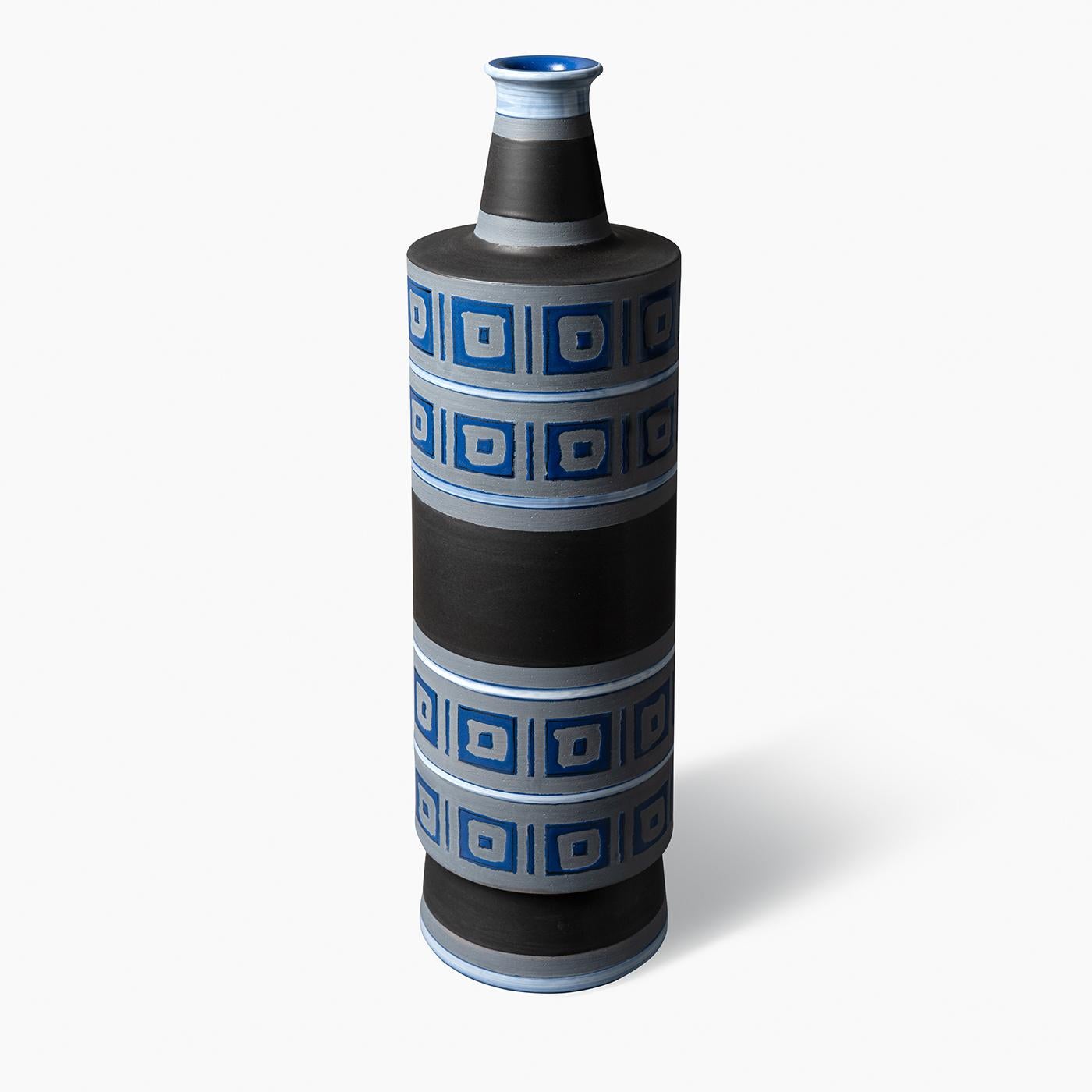 Ce vase décoratif présente une forme cylindrique réalisée sur un tour de potier en argile rouge. Sa surface est ornée de bandes horizontales alternant des motifs géométriques noirs et bleus mats inspirés des motifs grecs classiques. Faisant partie