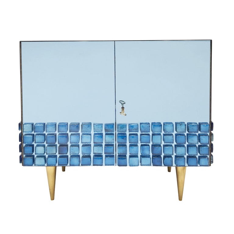 Limited edition cabinet made by Interno 43 for Gaspare Asaro. Features mirrored blue glass paneling with a fascia of blue glass medallions on the bottom. Brass legs and hardware with one glass shelf inside. It can be made custom in any size and