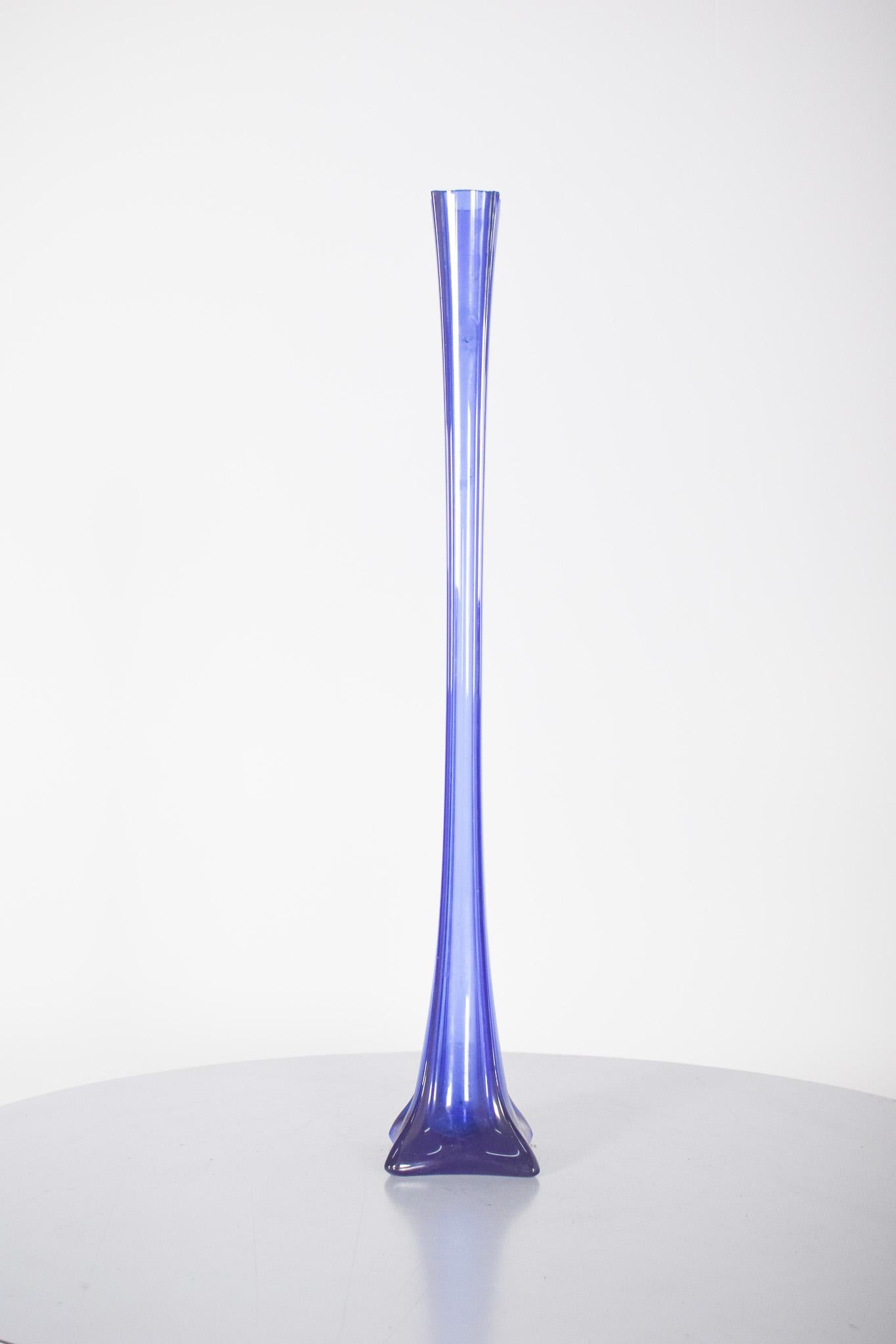 Solitaire en verre bleu. De forme allongée et étroite, c'est un vase idéal pour contenir une fleur unique à longue tige ou un petit arrangement floral. La base carrée légèrement incurvée assure la stabilité, tandis que le corps s'affine