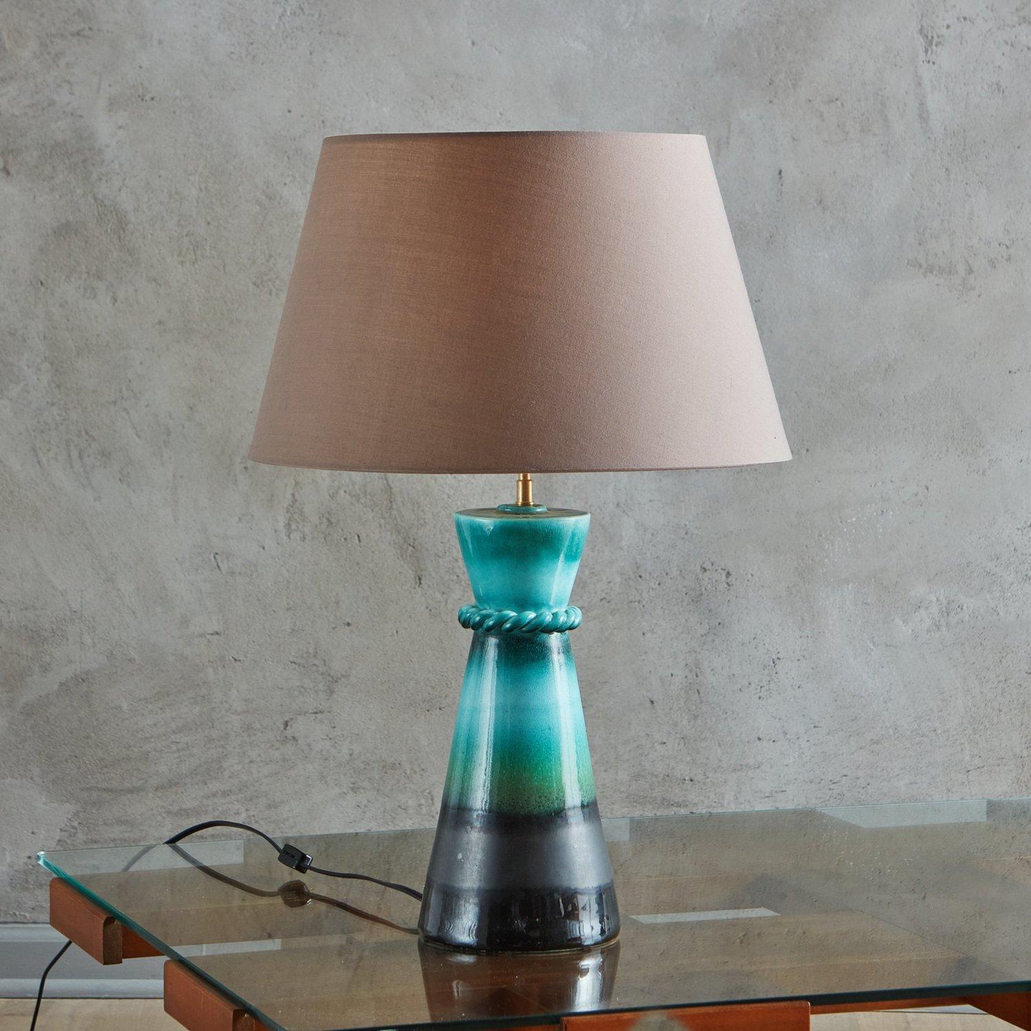 Eine französische Tischlampe aus den 1940er Jahren mit einem spitz zulaufenden, glasierten Keramiksockel in kräftigen Türkis-, Grün- und Schwarztönen. Diese Lampe hat eine dekorative geflochtene Verzierung und einen taupefarbenen Lampenschirm. Auf